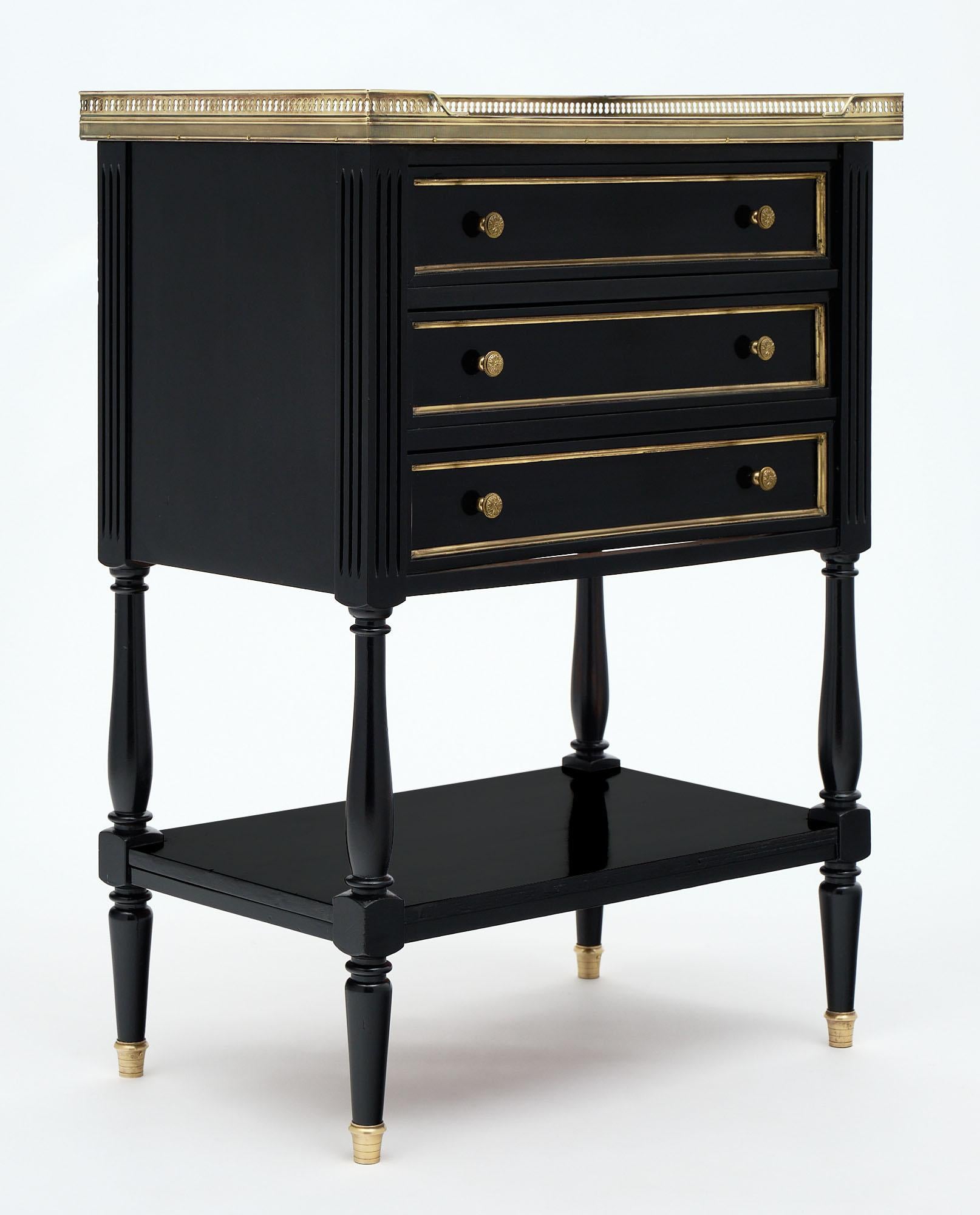 Louis XVI style French side table made of mahogany that has been ebonized and finished with a lustrous French polish. The cabinet features a white Carrara marble top surrounded with an open gilt brass gallery and gilt brass trims around the three