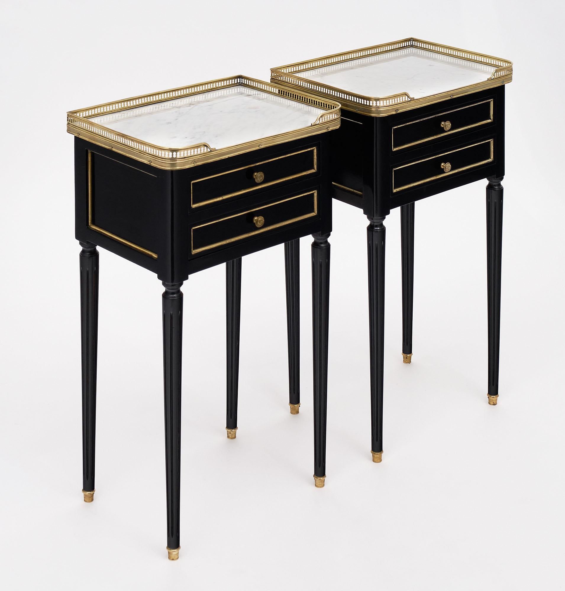 Pair of side tables, French, in the Louis XVI style with intact Carrara marble tops and opened gilt brass galleries. Each features two dovetailed drawers and fluted, tapered legs. The gilt brass trim throughout contrasts beautifully with the