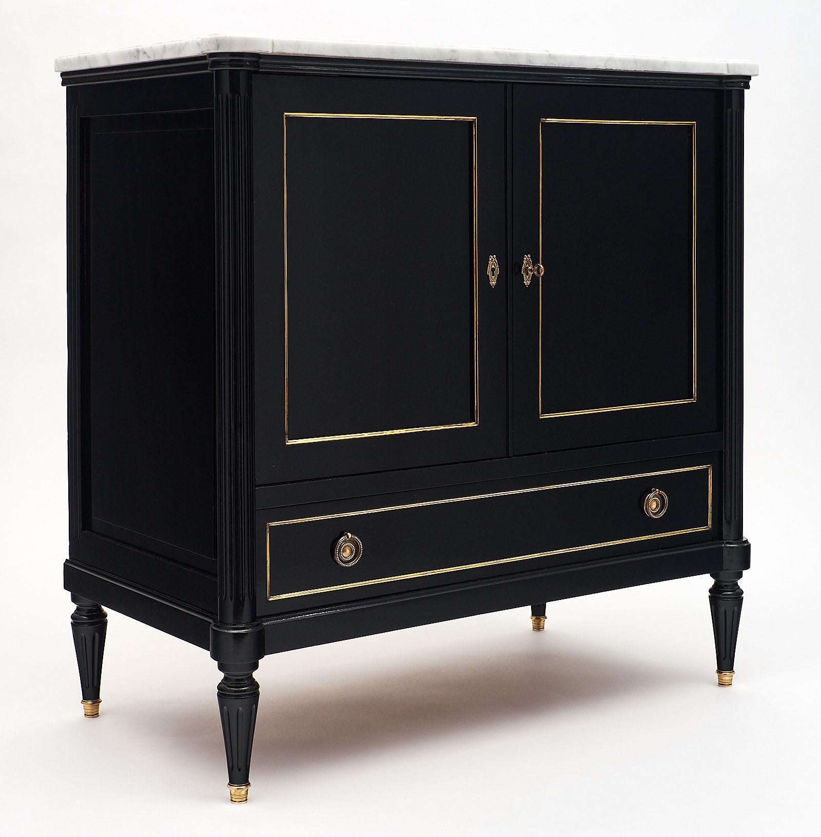 French Louis XVI style two-door buffet with a beautiful Carrara marble top. It is made of solid mahogany that has been ebonized and finished with a lustrous French polish. All of the brass trim and working hardware is original. We love the compact