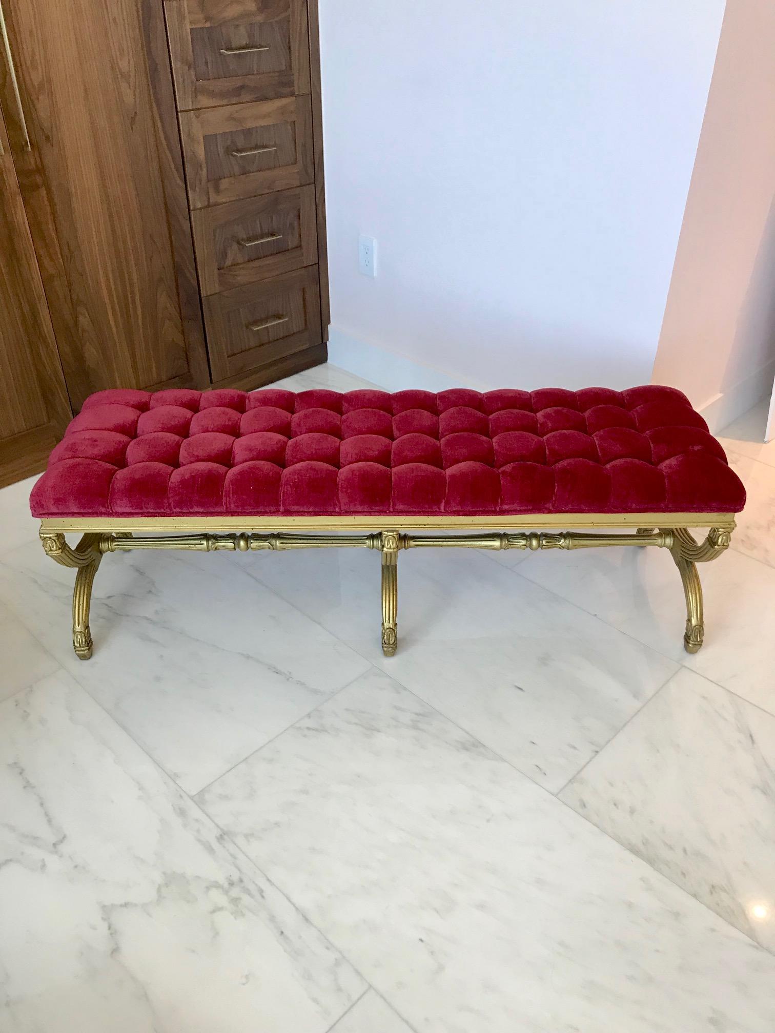 Elegant Venetian Louis XVI style long bench with giltwood frame. Features beautiful biscuit tufted seat in a deep red fabric. Base features series of ornate hand carved designs with antiqued gold leaf finish.
