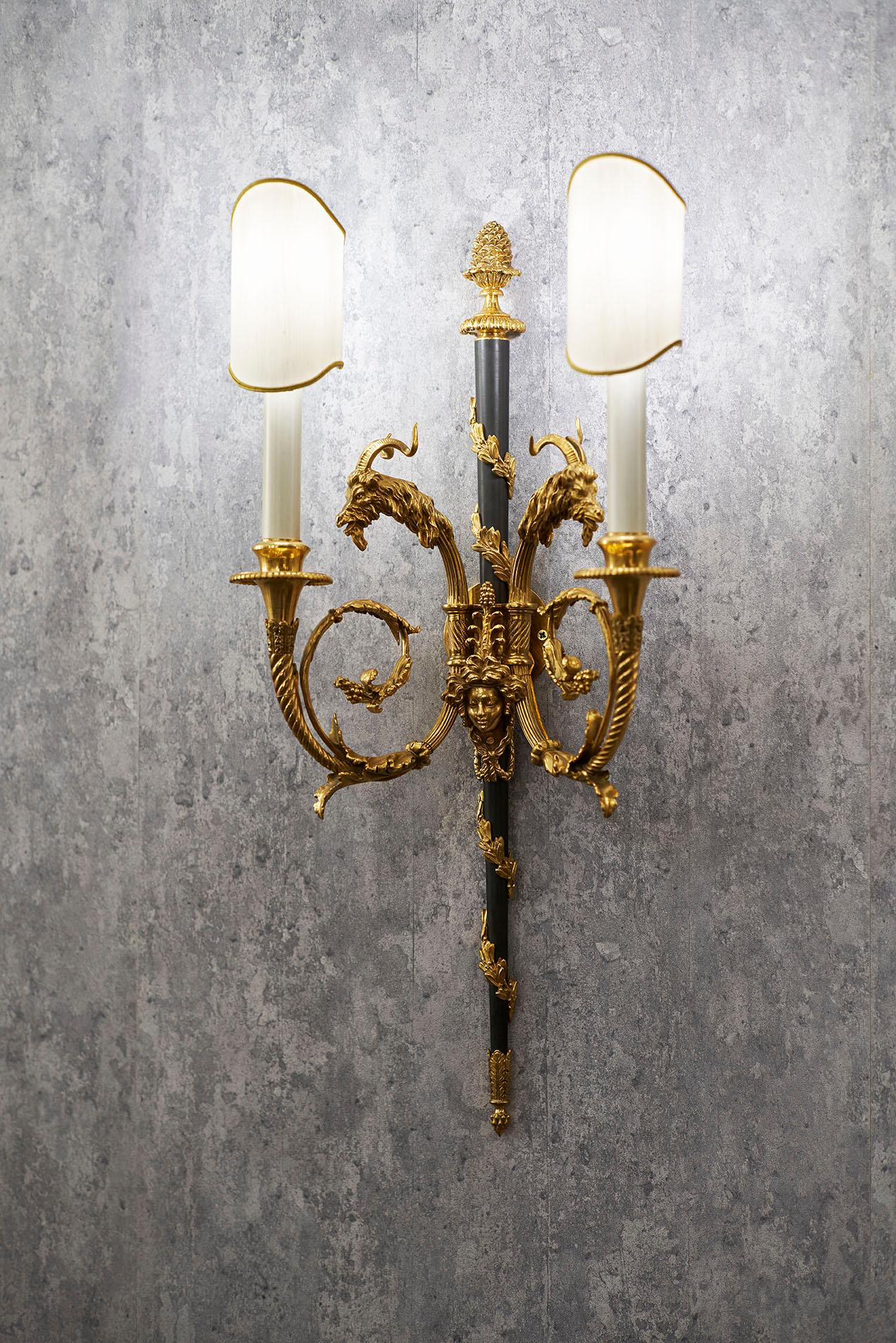 Este candelabro de dos brazos de estilo Luis XVI en bronce dorado y bruñido de Gherardo Degli Albizzi está centrado por una barra de bronce bruñido decorada con un motivo vegetal en espiral y un remate de pino. Los brazos muestran impresionantes