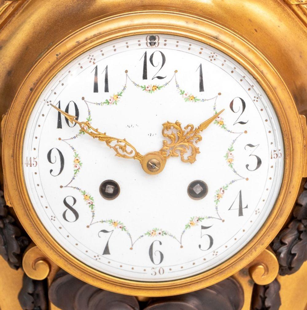Louis XVI Style Gilt and Patinated Bronze Clock, the circular painted enamel dial, with strike on bell movement, the cartouche shaped case mounted with a finial, acanthus and laurel swags centered by a brazier, on a conforming plinth and toupie