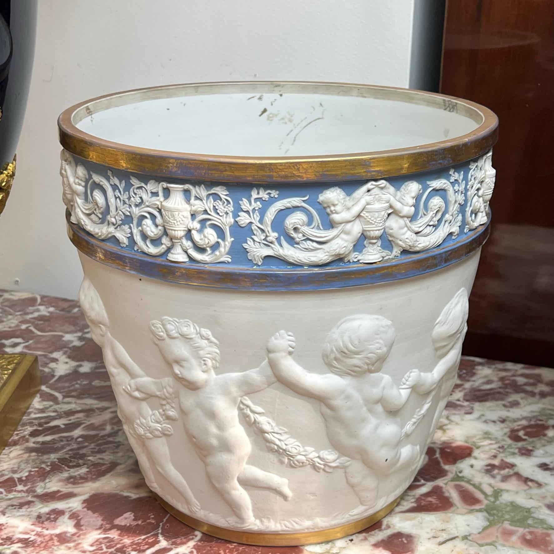 Our French jardiniere in the Louis XVI style dates from the late nineteenth century and features the figures of frolicking putti in relief, and jasperware band depicting neoclassical motifs in bisque on blue ground. A fine and large example of a