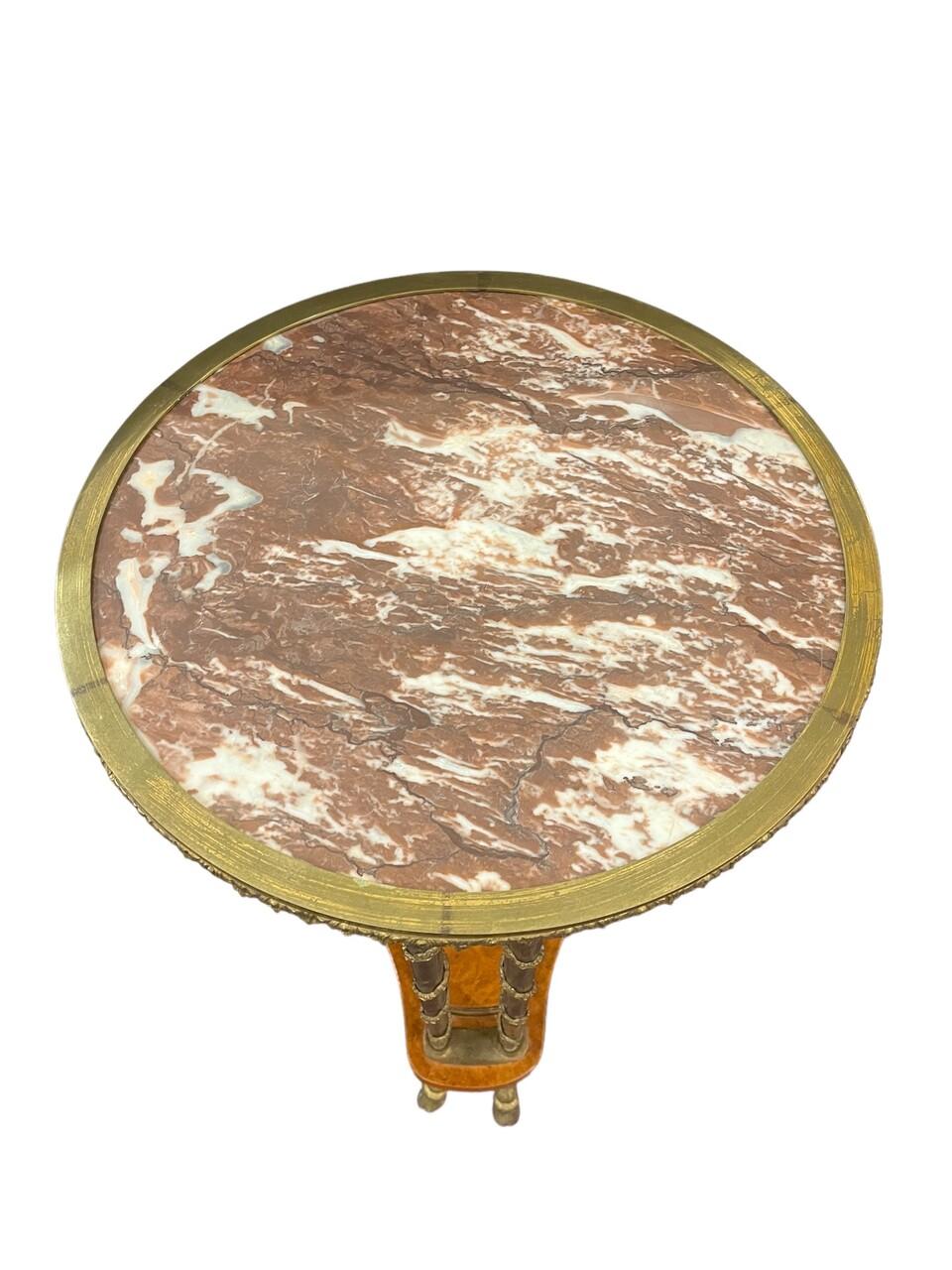Questo tavolo gueridon in stile Luigi XVI incarna un'eleganza senza tempo, realizzato con accenti in bronzo dorato e coronato da un lussuoso piano in marmo. Ispirato agli squisiti design di Adam Weisweiler, questo pezzo fonde perfettamente opulenza