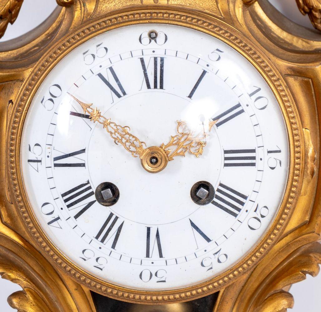 Orologio a cartello in bronzo dorato in stile Louis XVI, metà del XIX secolo. Il quadrante circolare in smalto bianco, con movimento a campana, è sormontato da un centrotavola coperto da due manici che trae ghirlande di acanto, con il marchio