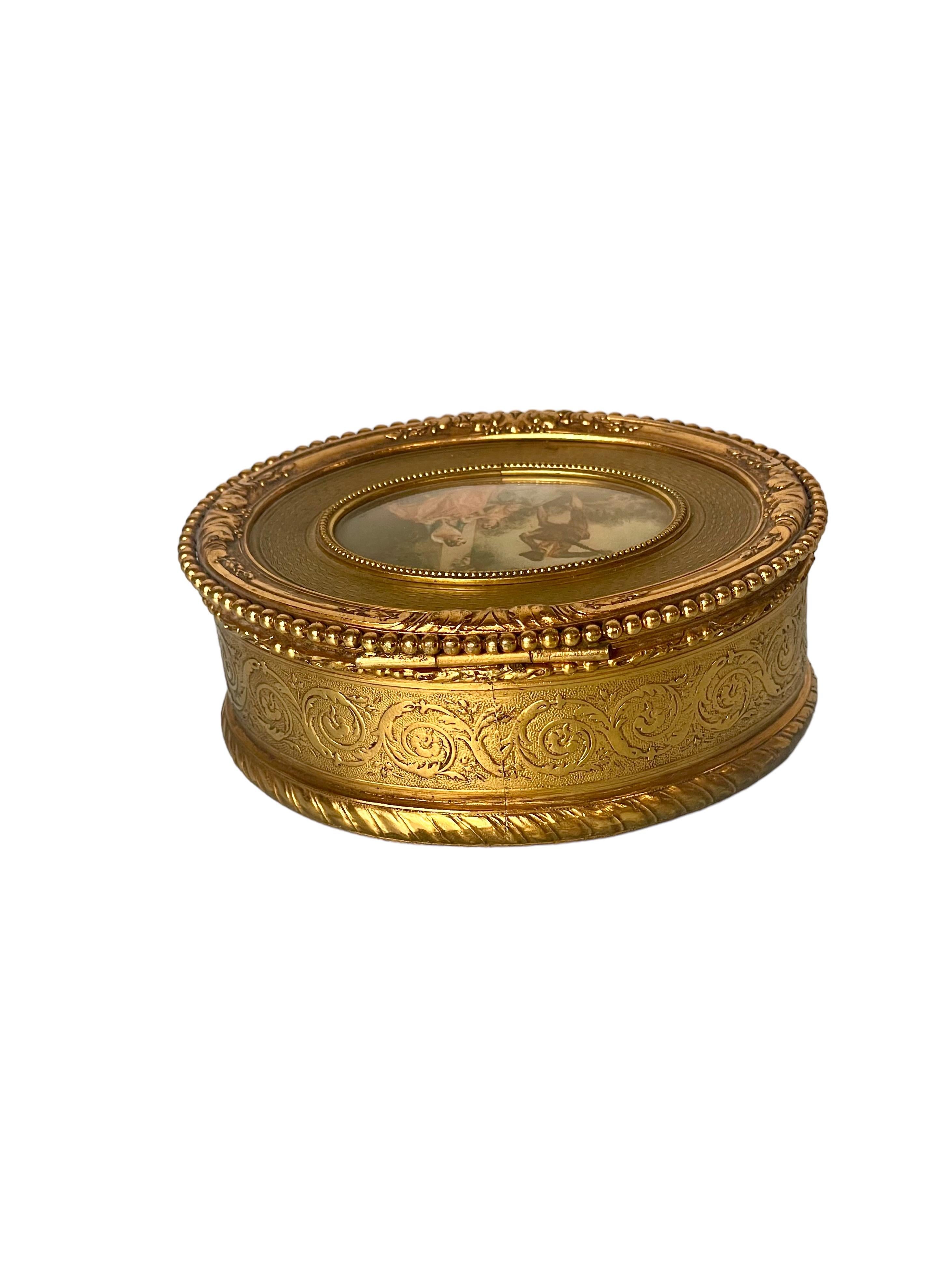 Très jolie boîte à bijoux de forme ovale en bronze doré, avec une exquise miniature centrale représentant un jeune homme jouant la sérénade à deux jeunes femmes avec un luth. Ce coffret de style Louis XVI est étonnamment détaillé avec un motif