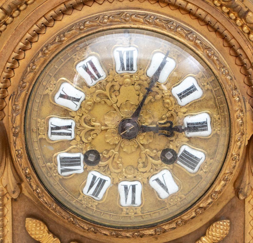 Orologio da caminetto in bronzo dorato in stile Luigi XVI, fine del XIX secolo, sormontato da un'urna che emette una corona d'alloro, il quadrante circolare con numeri smaltati, il movimento a campana, fiancheggiato da colonne affusolate, trofei