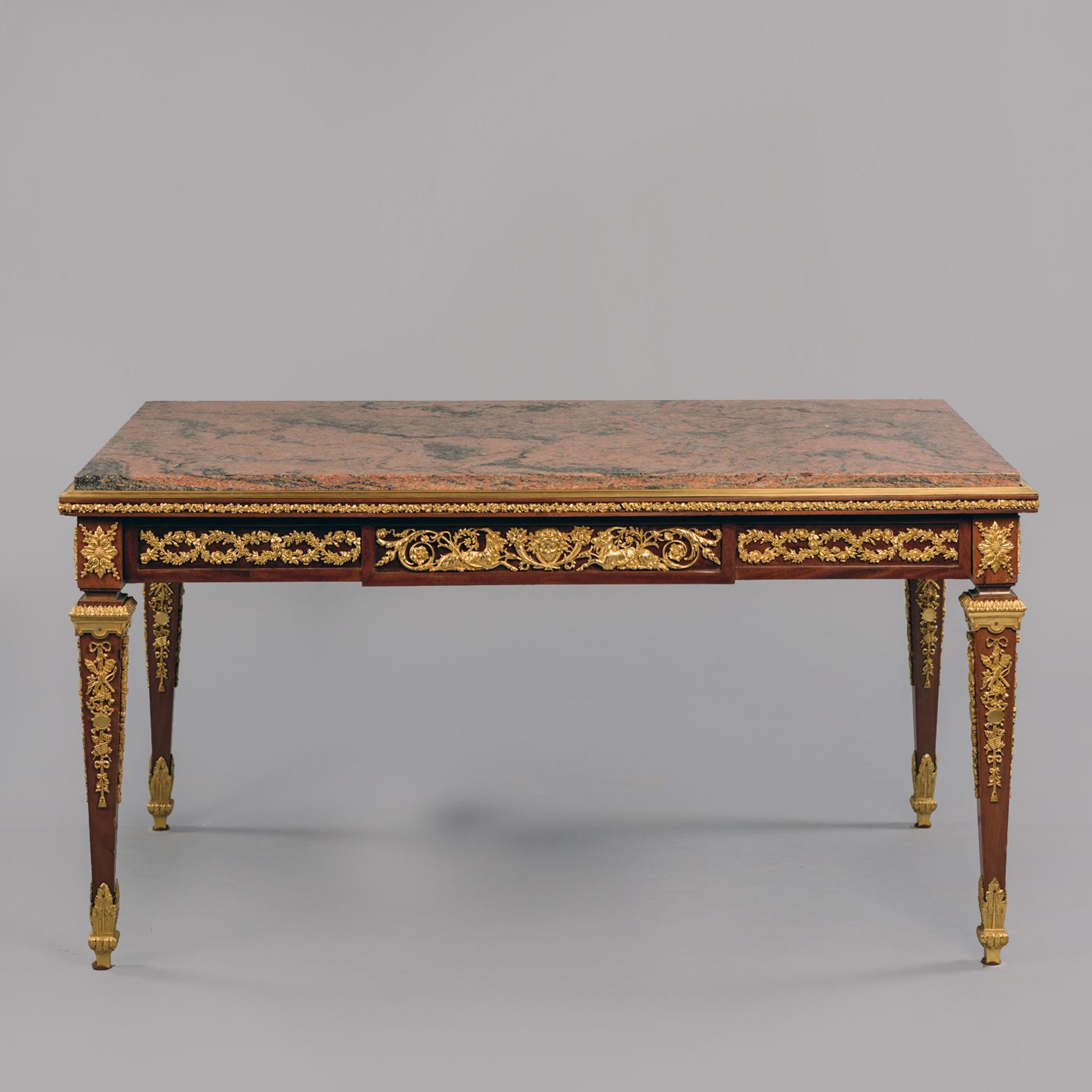 Table basse de style Louis XVI en bronze doré avec un plateau en marbre rouge veiné.

La table présente un plateau rectangulaire en marbre rouge veiné, surmonté d'une frise à décor de feuillages, centrée par une tablette ornée d'acanthes, d'un