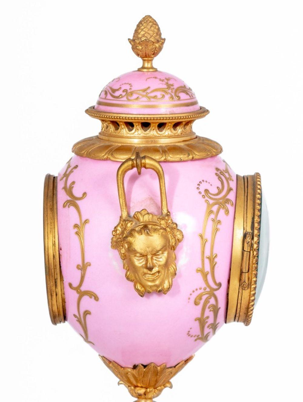 Louis XVI Style Sevres Gilt Bronze Mounted Pink Ground Three Piece Clock Set, late 19th century, the clock centered by a white enamel dial painted with flowers, two handles with masque heads, cassolettes with flambeau finials reversible to
