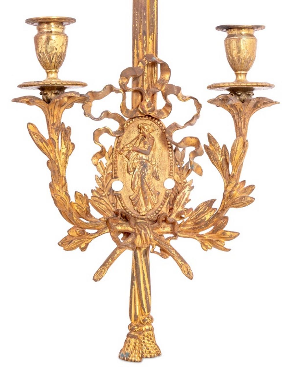 Coppia di applique gemelle in metallo dorato in stile Luigi XVI, inizio XX secolo, ciascuna con decorazione di rami intrecciati e nastri, centrata da un medaglione ovale di una donna che suona la pipa. 23,25
