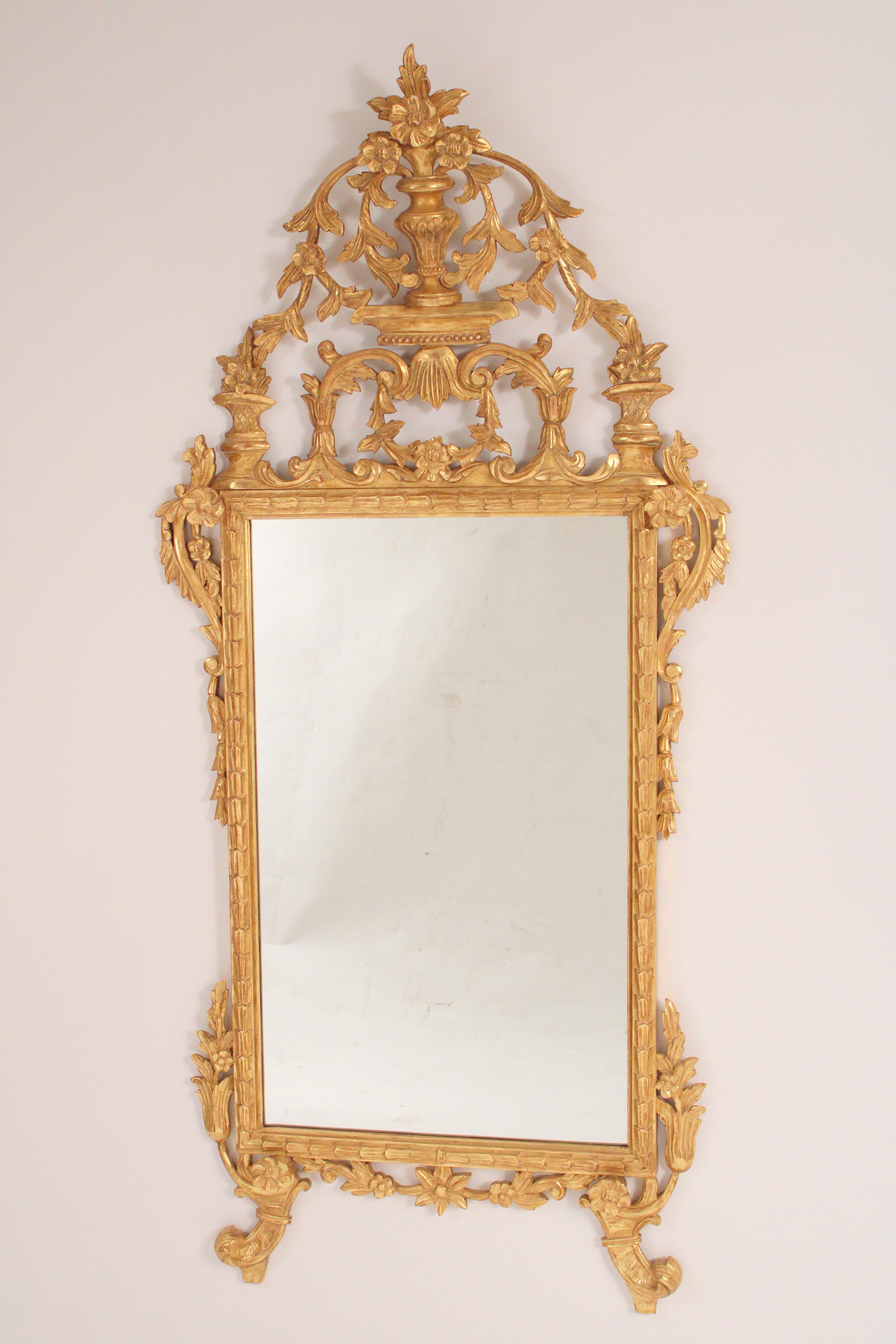 Louis XVI style gilt wood (gold leaf) mirror, circa 1960.  Very well done pediment with a vase out of which are flowing flowers and leaves, the sides with s shaped appliques and bell flowers the bottom border with carved flowers.