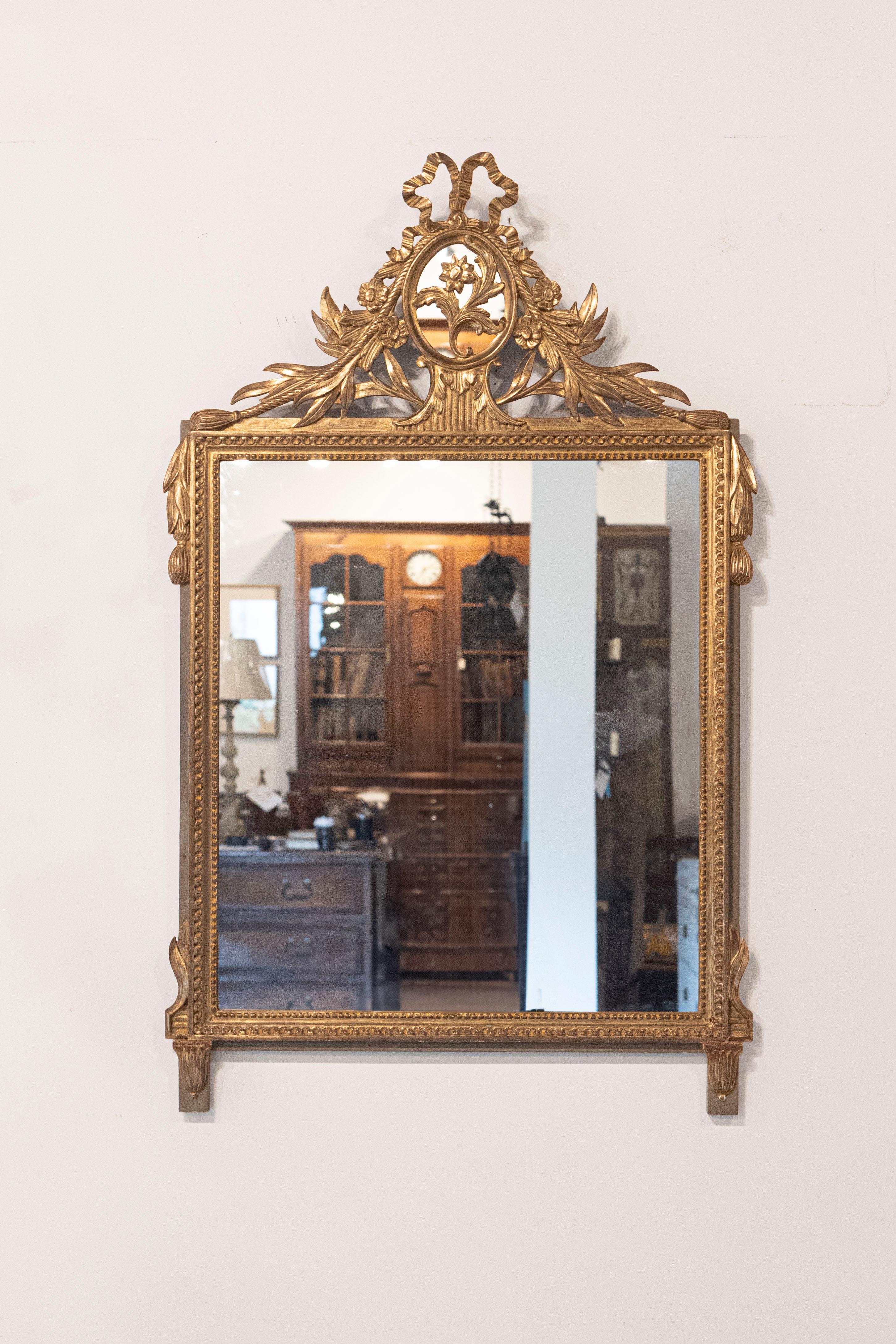 Miroir en bois doré de style Louis XVI, datant du 20e siècle, avec médaillon floral noué par un ruban, petites perles sculptées et glands. Exhalant la grâce et la grandeur de l'artisanat français, ce miroir en bois doré de style Louis XVI datant du