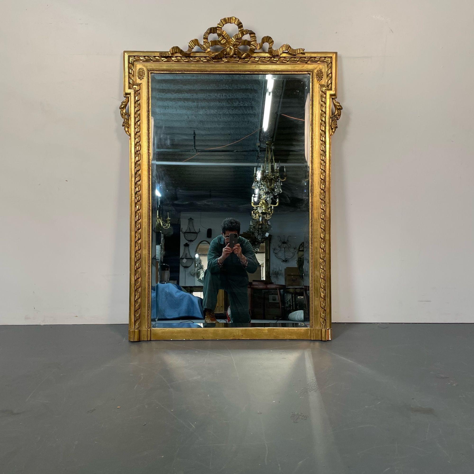 Miroir mural en bois doré de style Louis XVI, fin 19ème début 20ème siècle. 
 
Un grand et impressionnant miroir mural ou de console avec un miroir biseauté propre au centre flanqué d'un cadre doré à l'eau 24 kt représentant des motifs de glands,