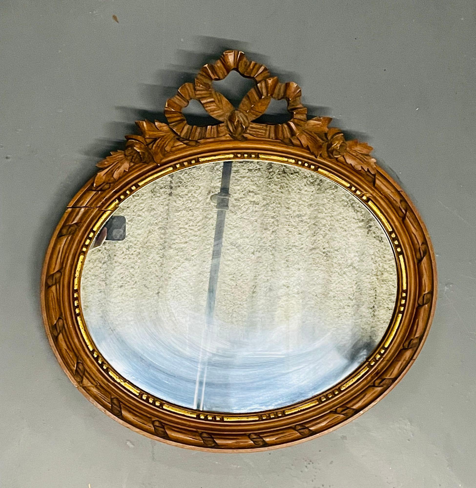 Louis XVI style gilt wood wall or console mirror
A sleek French oval gilt wood wall mirror having a clean center mirror panel framed in a gilt decorated frame terminating in a ribbon with bow and floral design. 
Measures: 23.5H x 24W.