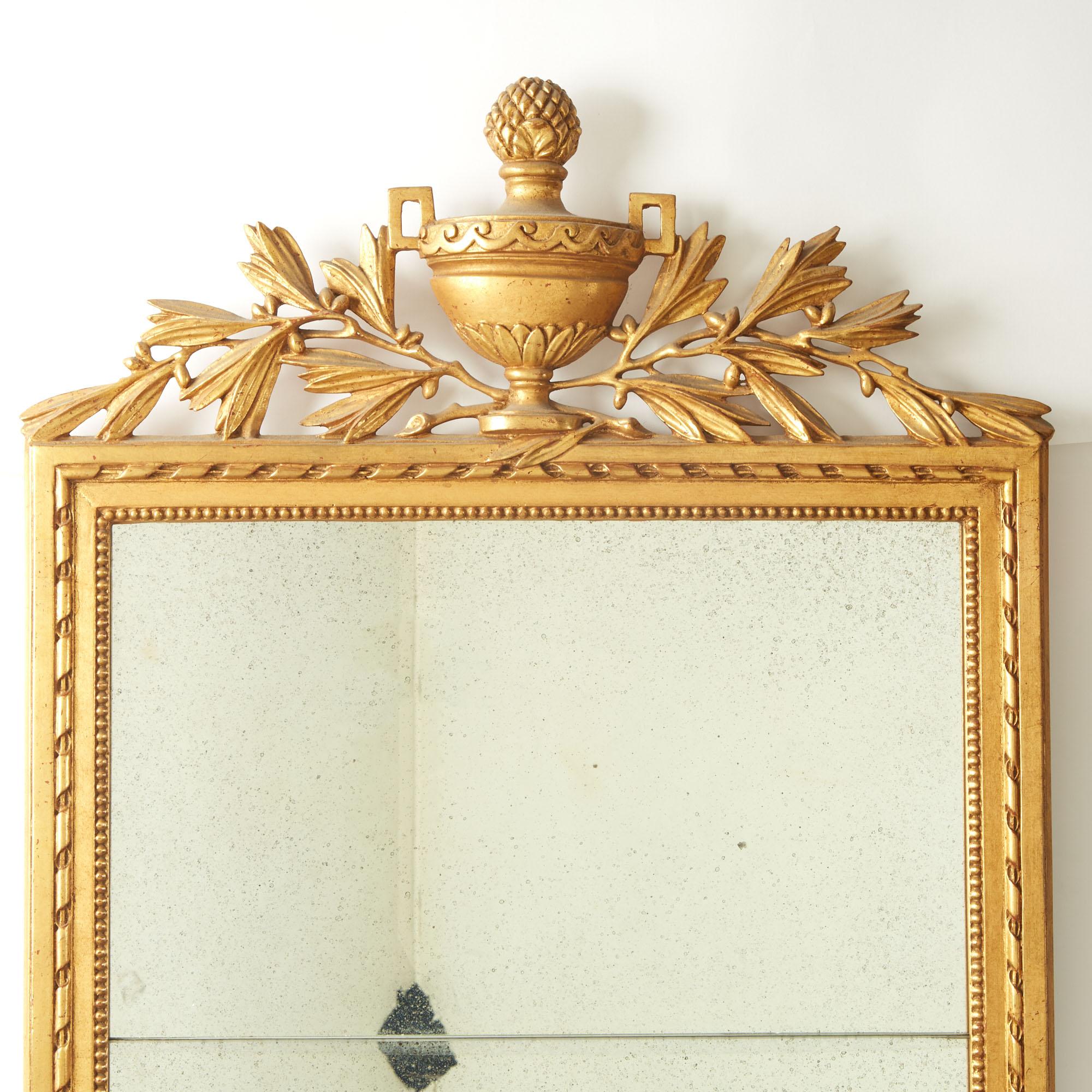 Ce magnifique  Le miroir mural de style Louis XVI est un véritable chef-d'œuvre de l'artisanat italien. D'une taille impressionnante, le miroir est orné d'une couronne de bois doré sculptée de façon complexe, ce qui lui confère une élégance