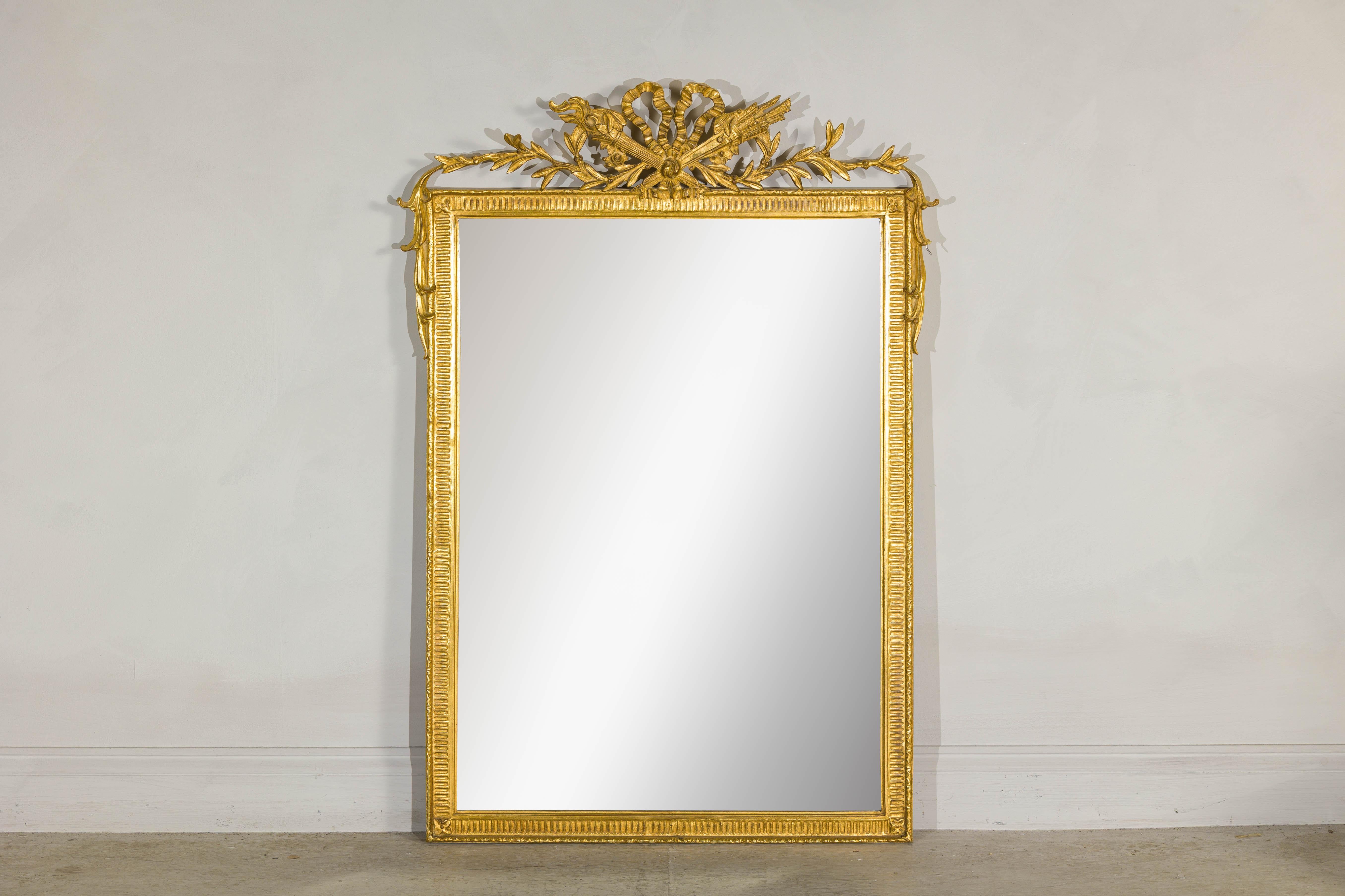 Crowned with a sculptural crest that speaks the language of allegory, this Louis XVI-style giltwood mirror offers more than reflection—it evokes the grandeur and ideals of the Enlightenment. At the summit, a knotted ribbon binds together a flaming
