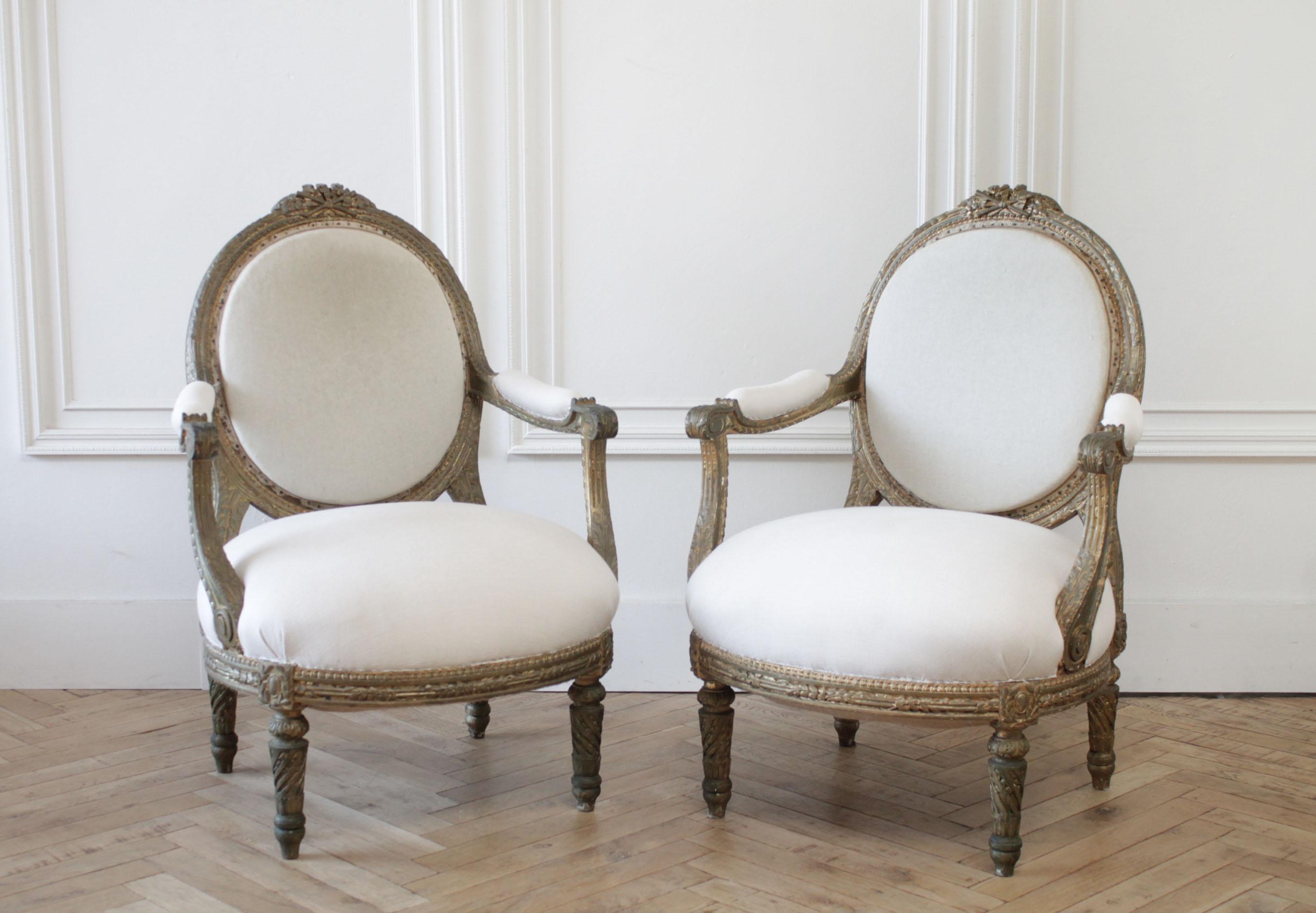 Louis XVI style giltwood open armchairs.
The back is original muslin upholstery, with nail trim, and the seats are upholstered in a light natural oatmeal linen. The frames are solid and sturdy, ready for everyday use. Gilt wood finish has age and