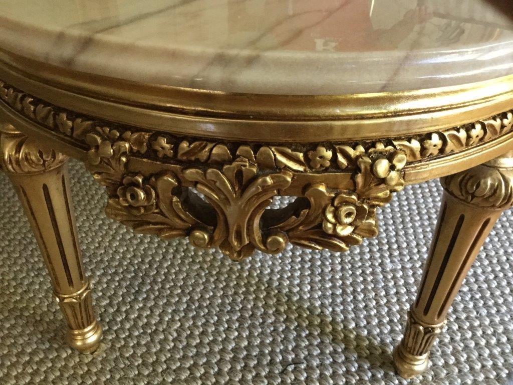 Elegant Louis XVI style carved gilt coffee table with a beautiful beveled marble top. This table, made in Italy, is oval and features a carved and finely base with a light gold marble top. Excellent condition.