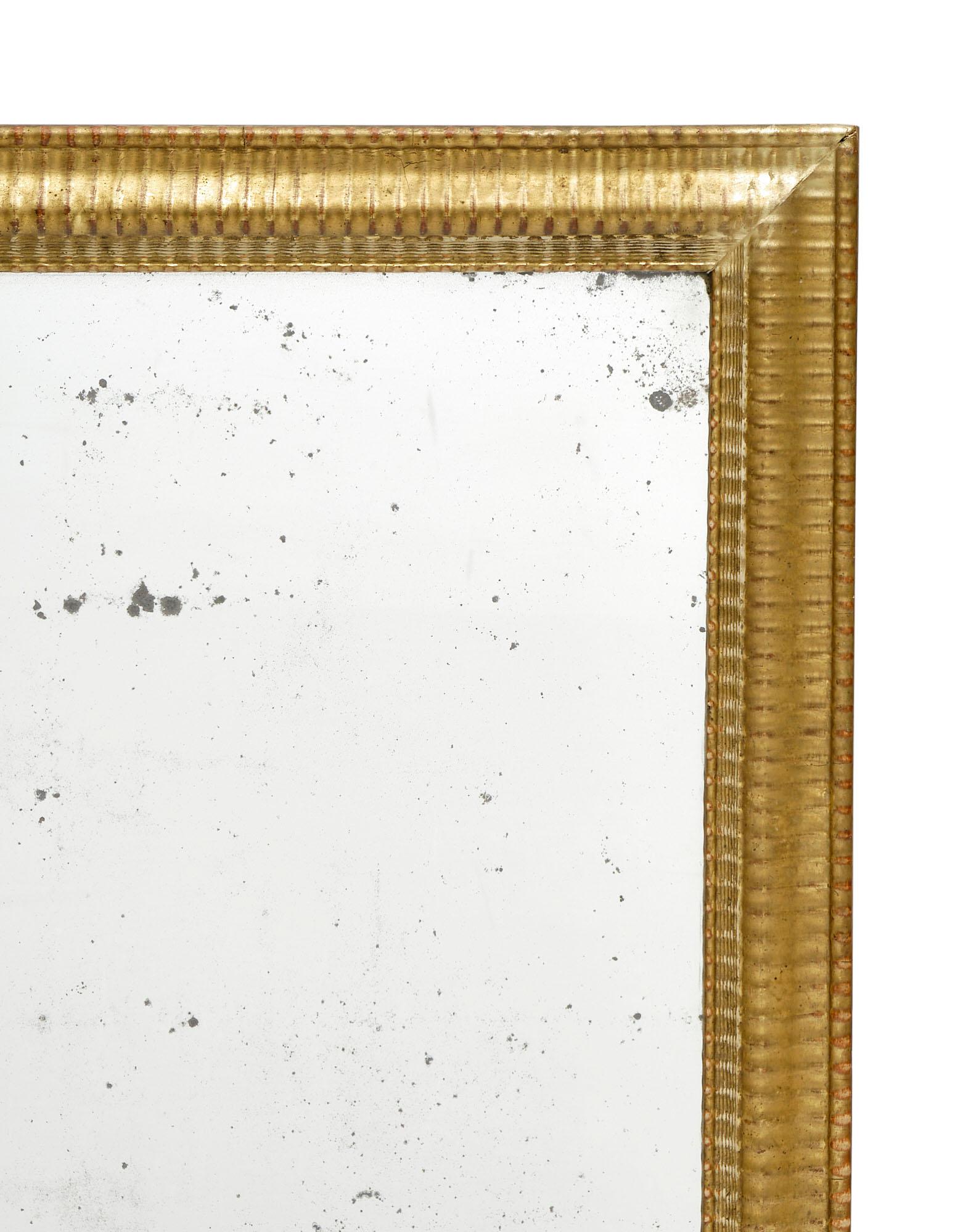 Rectangular mirror featuring the original mercury mirror and an elegant gold leafed frame. The frame has an undulating hand-carved texture with a beautiful, original patina. The terra cotta color shows through the beautiful gold leafing.