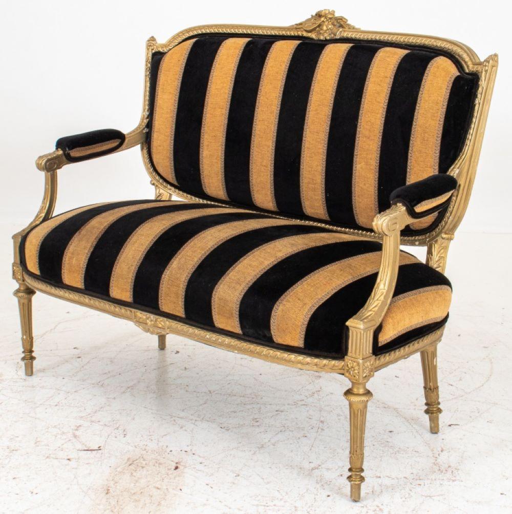 Louis XVI Style gold-painted marquise or settee, the shaped crestrail centering a musical trophy within an entrelac frame and upholstered back with downscrolling arms, with shaped rectangular seat above turned stop-fluted legs on toupie feet.
