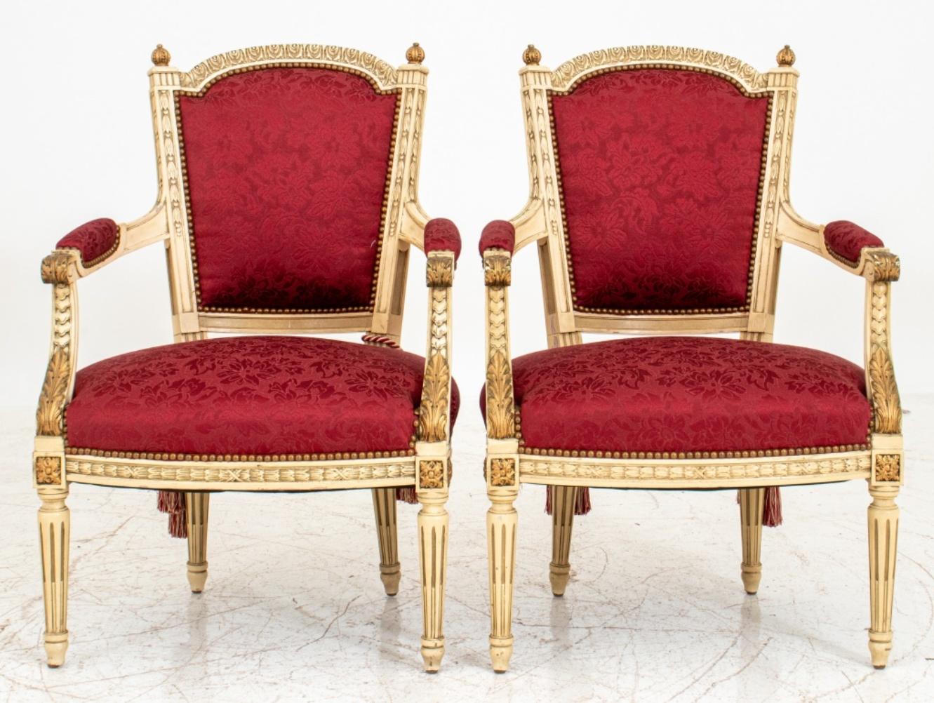 Pair of Louis XVI style red damask upholstered gold and white painted arm chairs or fauteuils de la reine en cabriolet, with arched crest rails and gilt finials above upholstered backs and down swept scrolling arms above a shaped rectangular seat