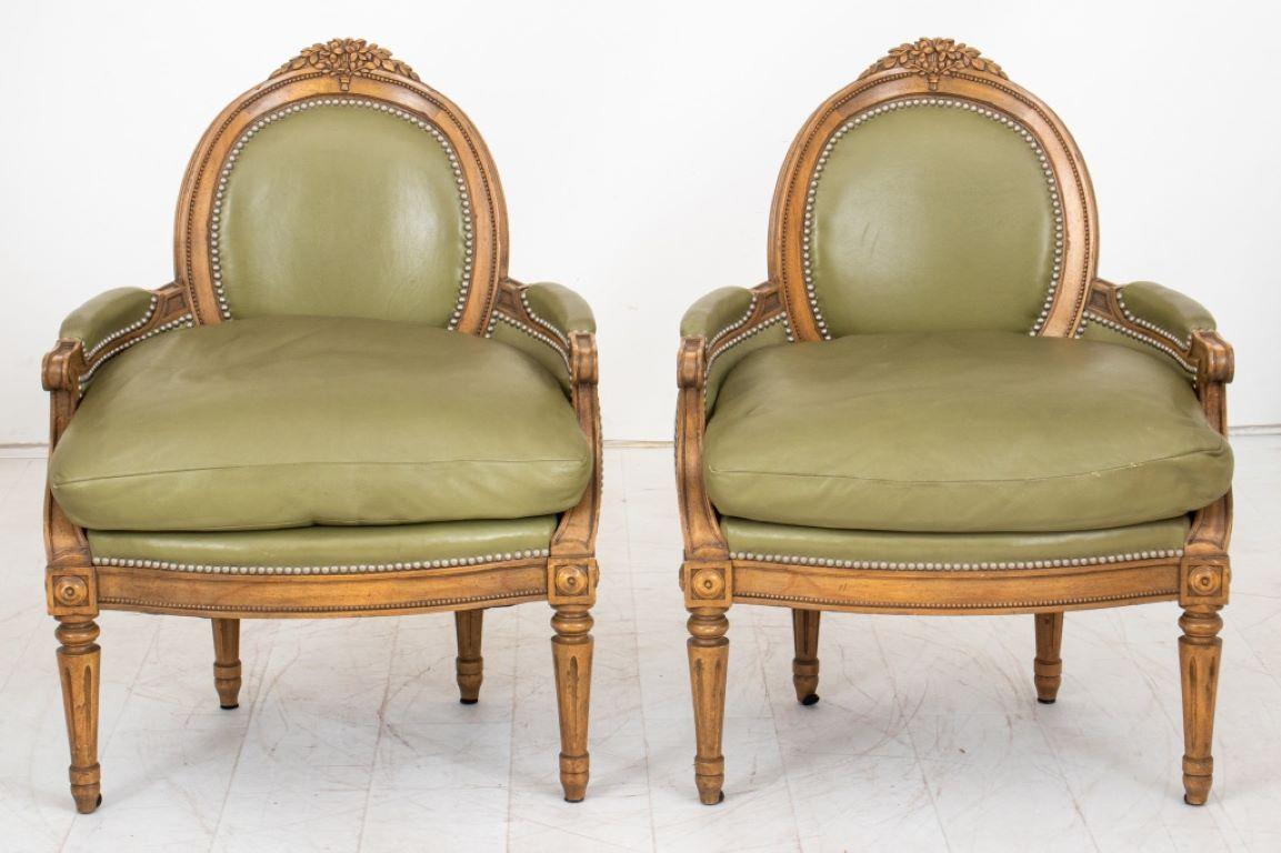 Pair of Louis XVI Style Walnut and Green Leather Upholstered Arm Chairs, or bergeres en corbeille, each with floral carved crestrail above an oval upholstered back, the arms incurved and with drop in seat cushions above a molded seat rail on paterae