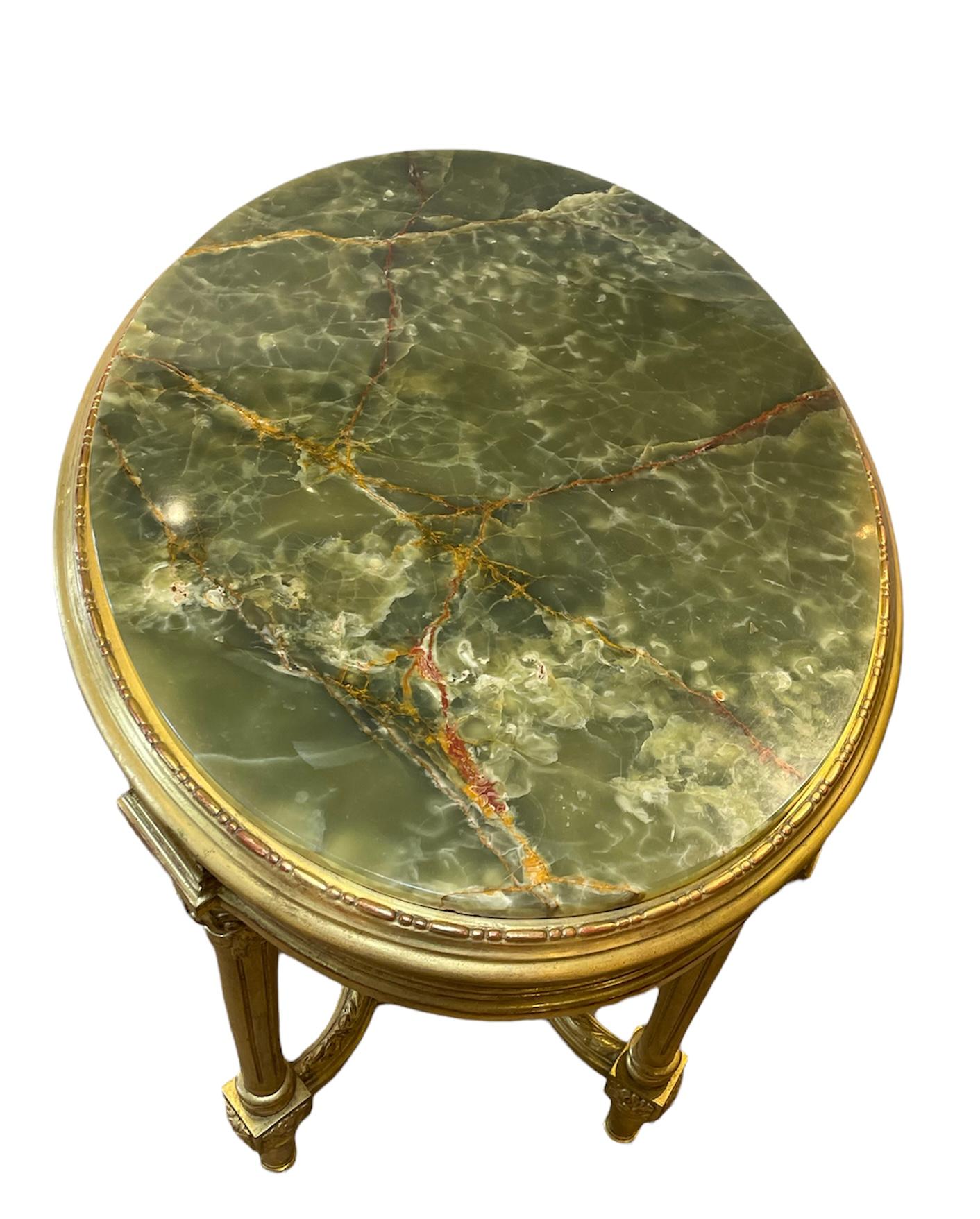This is a Louis XVI gilt wood and green onyx oval top center table. The upper border of the table is decorated with a link of reticulated rings alternated by squares with a carved flower. Below the border there is a small apron made of scrolls of