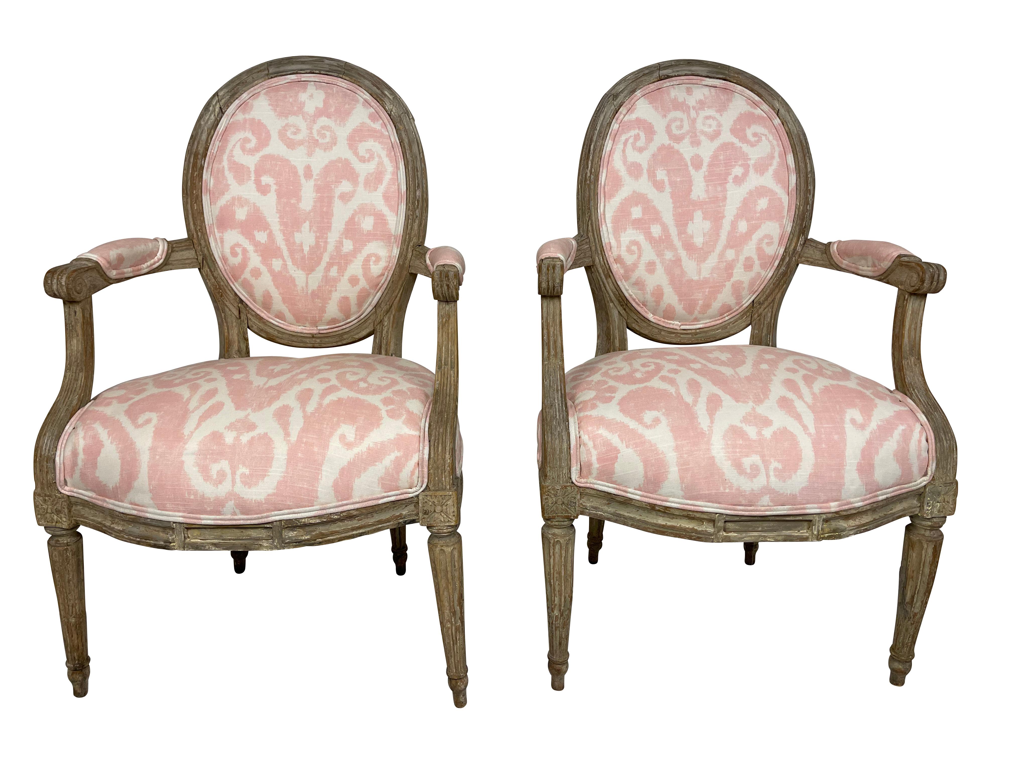A pair of diminutive size Louis XVI style original grey paint, and carved armchairs, newly reupholstered in a modern pink and white Ikat fabric. Oval backs, reeded legs with rosette decoration. Perfect for a bedroom, bathroom, or child's bedroom.