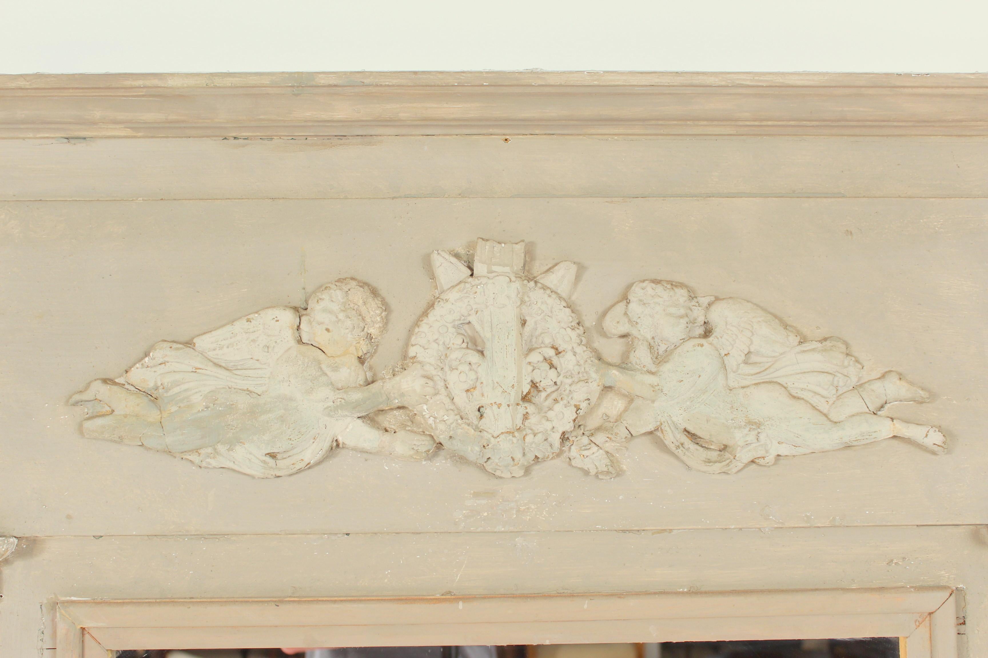 Louis XVI style grisaille painted wall mirror, circa 1910. Upper center area of mirror with two composition cupids holding a trophy and columns flanking either side of the mirror.