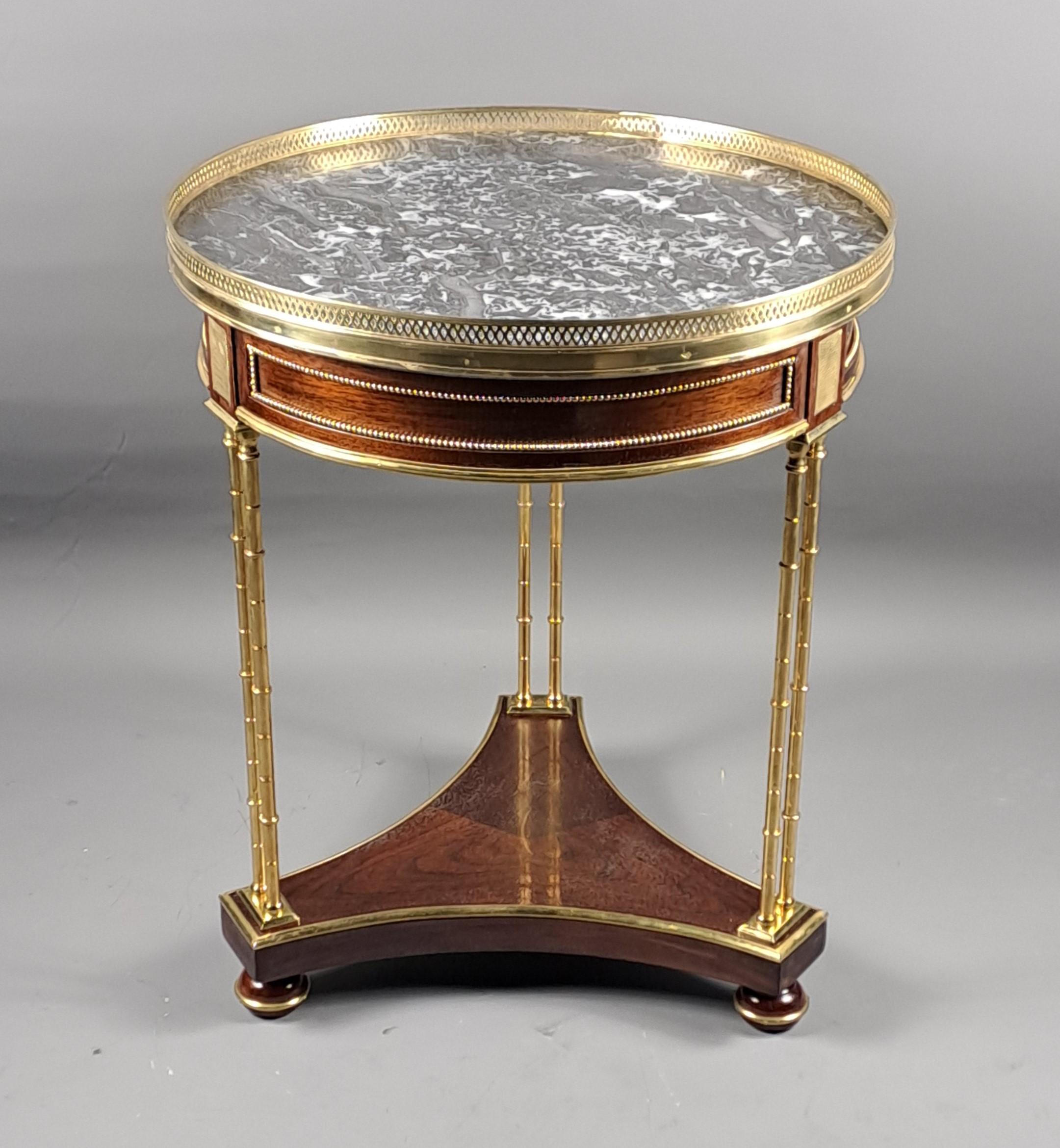 Mahogany veneer pedestal table, tripod base with a top-mounted crossbar topped with three double gilt bronze tube legs, Saint Anne grey marble top surrounded by an openwork brass gallery.   

Louis XVI style work based on a model by Adam Weisweiler.