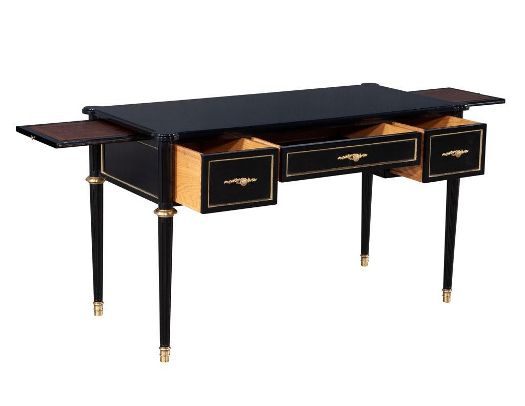 Louis XVI style high gloss black lacquered writing desk. American, circa 1950’s. Composed of solid woods with original brass ornament details. Side pullout trays offer added surface area with beautiful leather top detail with gold embossing. Desk is