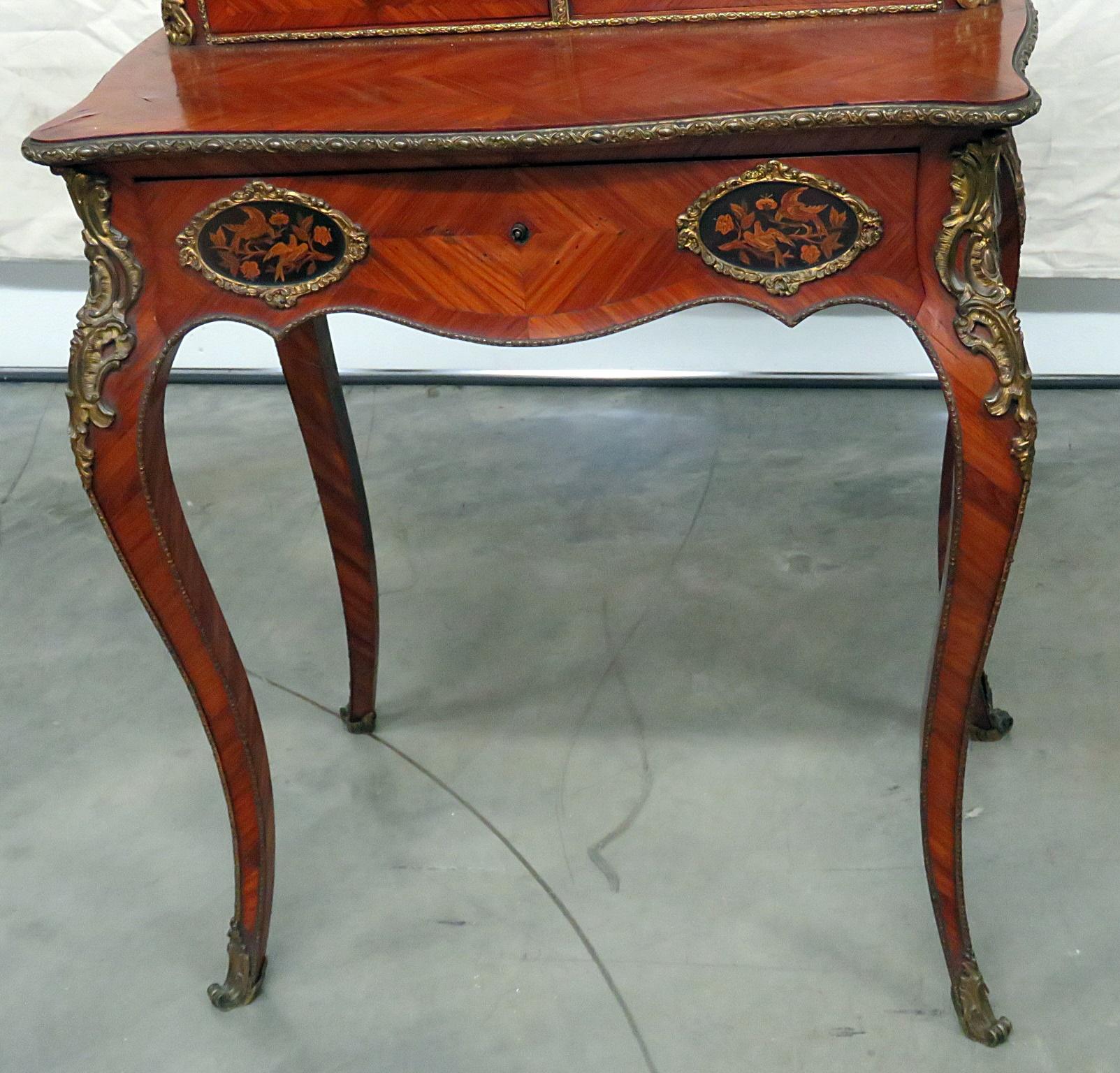 This is a superbly crafted 1870s era ladies writing desk with a cartonnier shelf compartment above the writing surface. The desk features incredible bronze ormolu and inlaid mixed woods. There are very few of these available and this is a very