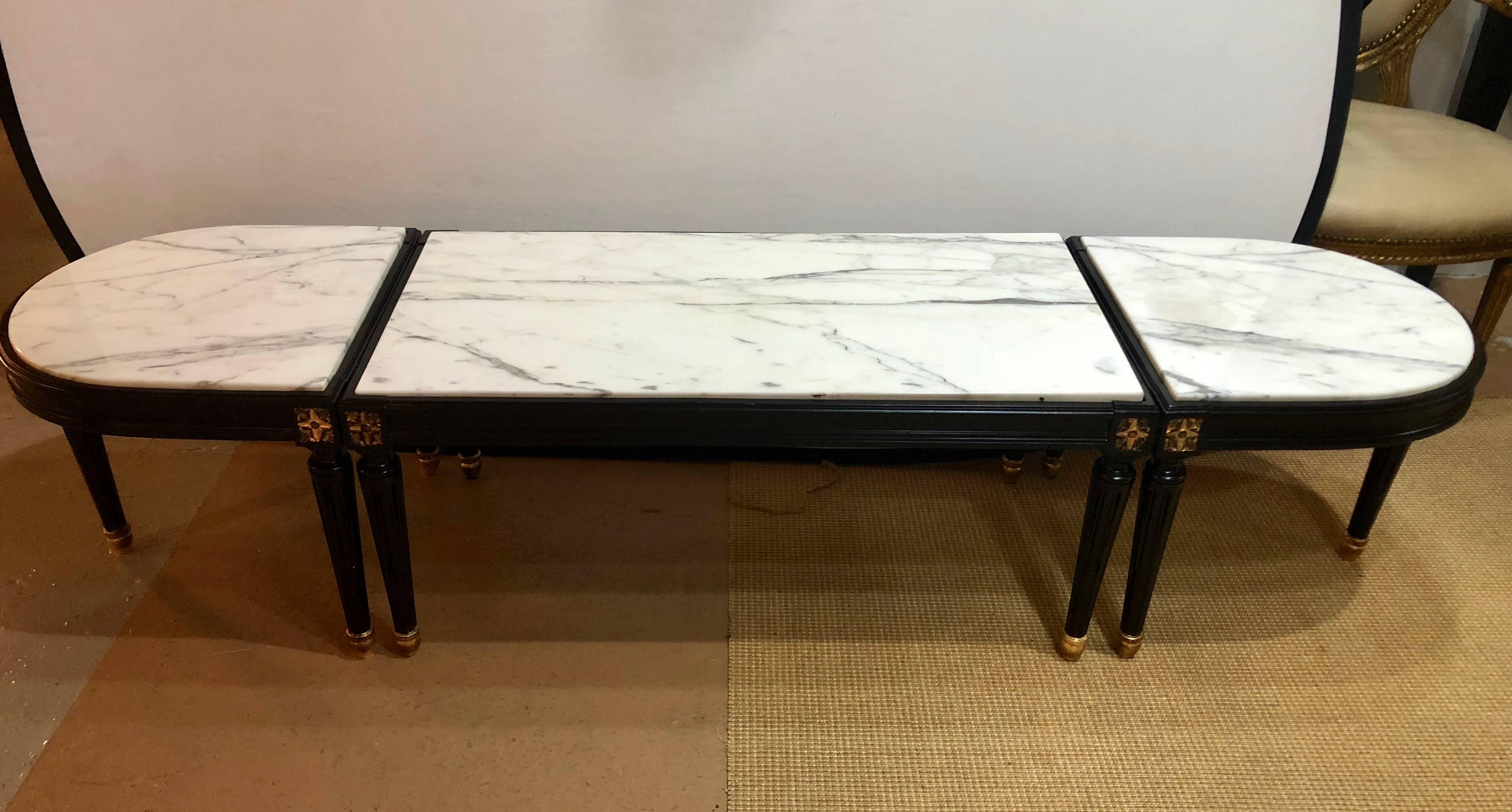 A Louis XVI style inset marble-top three-piece coffee table in the manner of Maison Jansen. This ebony and parcel-gilt decorated coffee table can be sitting placed together or used as a center coffee table and two end tables or stands. Each white