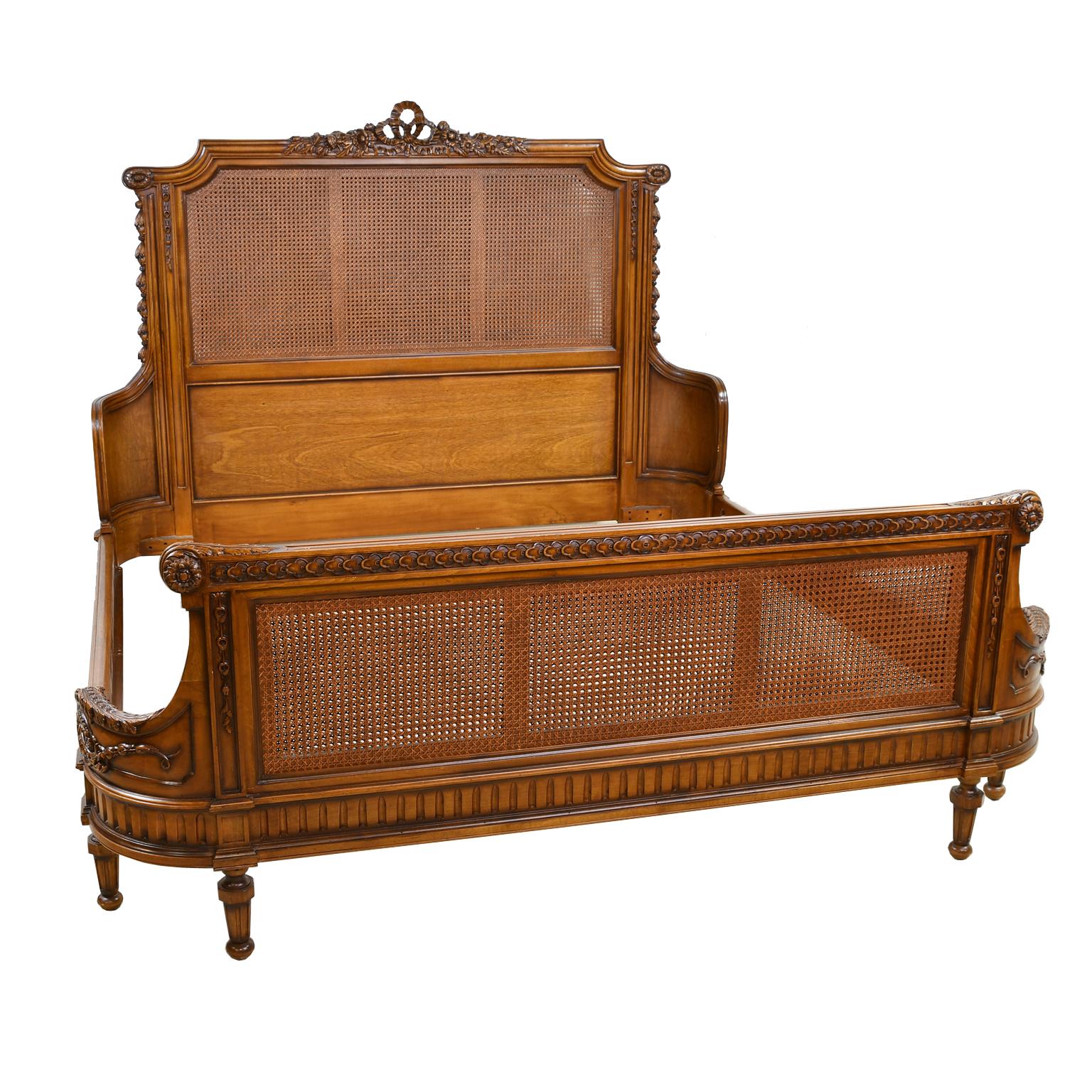 A lovely and beautifully-crafted reproduction Louis XVI style bed frame in king size in a medium-colored hardwood that looks like walnut, with caning on the frame's headboard and footboard which are rounded at the corners. Carved embellishments