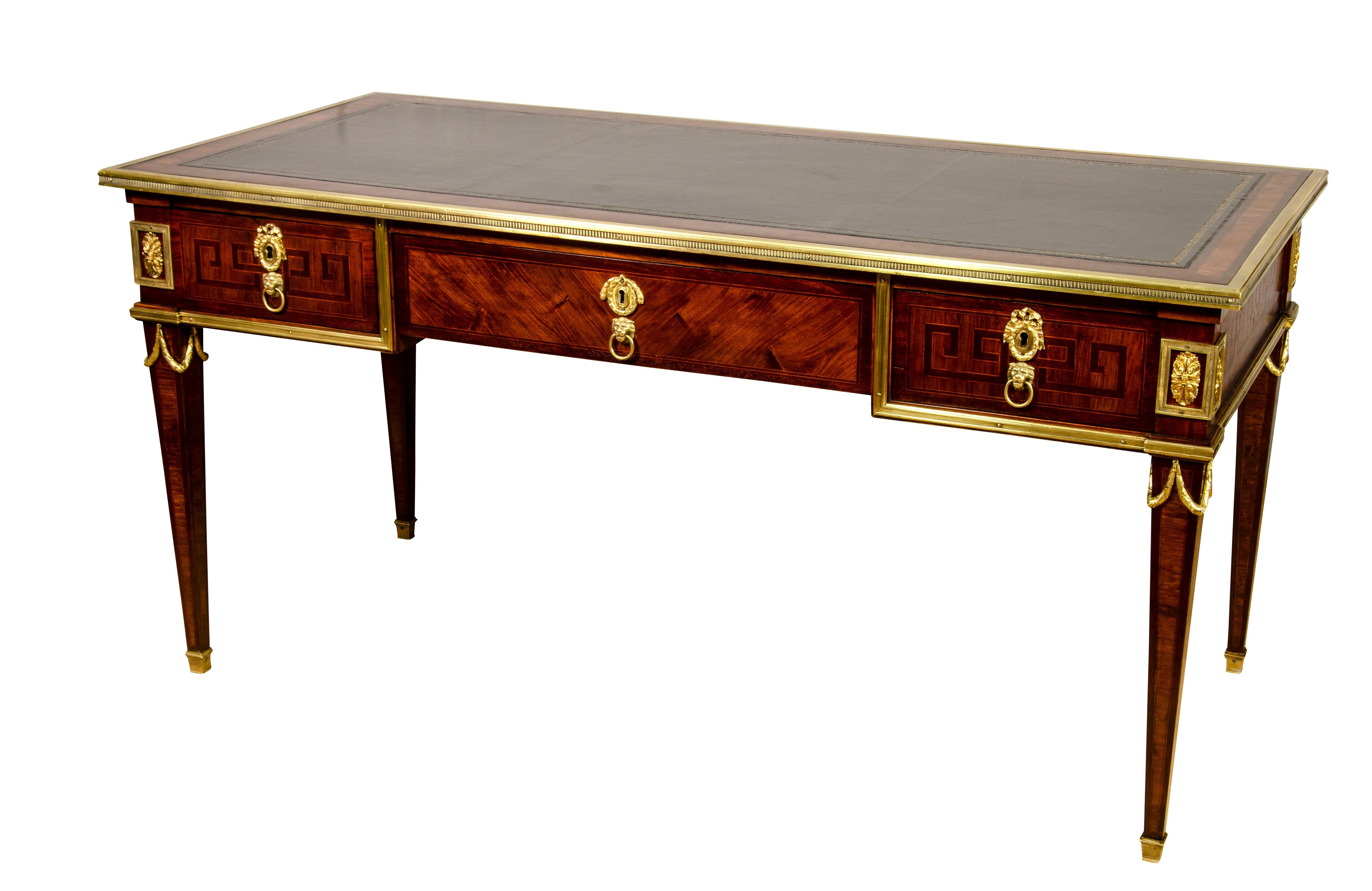 Rectangular inset tooled black leather top with cross banded edge and brass border over a frieze with a central and two flanking drawers, raised on square tapered legs headed by gilt bronze mounts , back finished to stand freely in a room.