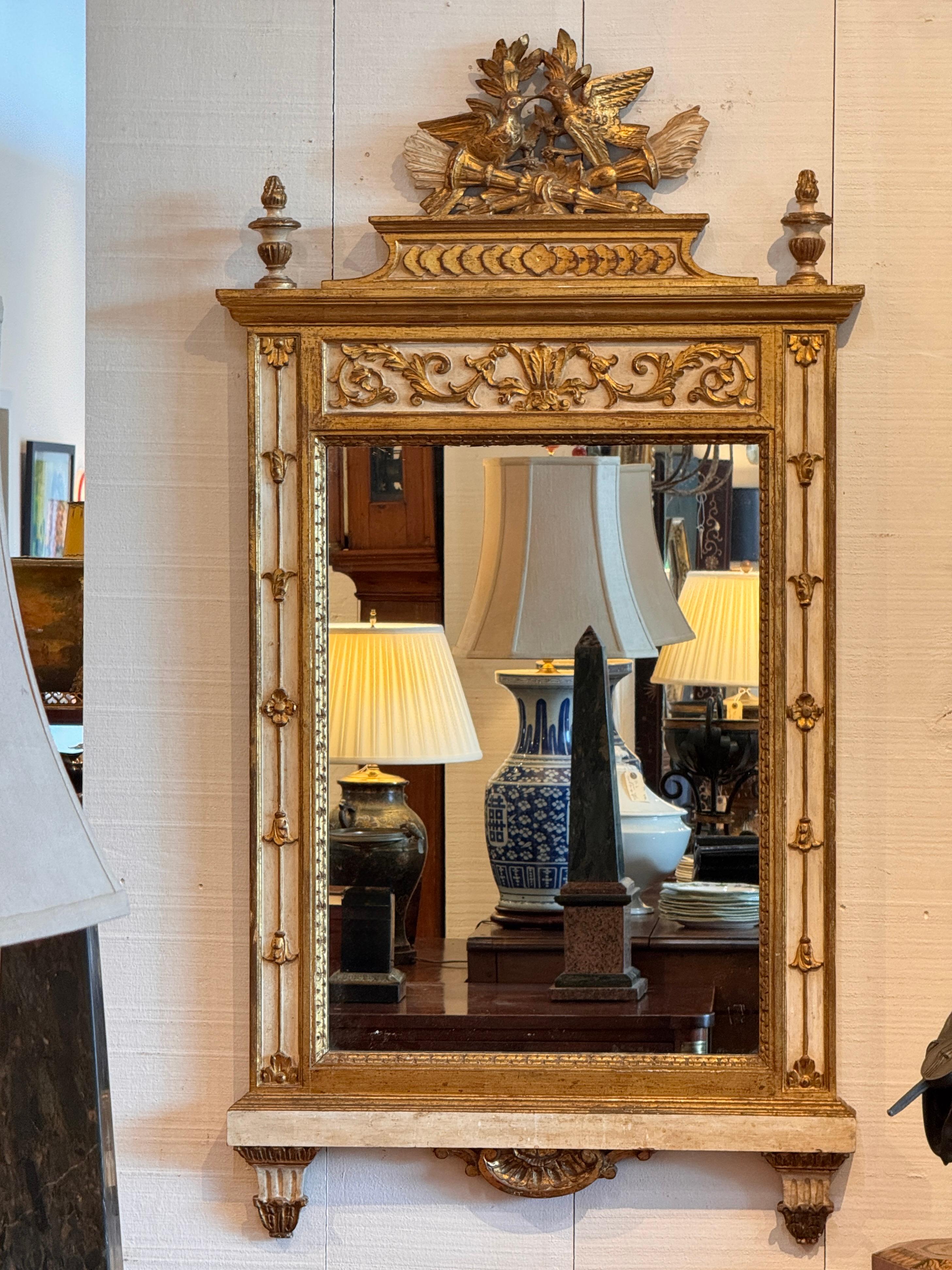 Spiegel im Louis XVI-Stil von LaBarge mit geschnitztem und vergoldetem neoklassizistischem Wappen mit Vögeln und Musiktrophäen. Der Rahmen ist in einem sanften Cremeton mit vergoldeten Akzenten und Akanthus-Details entlang des Frieses bemalt.