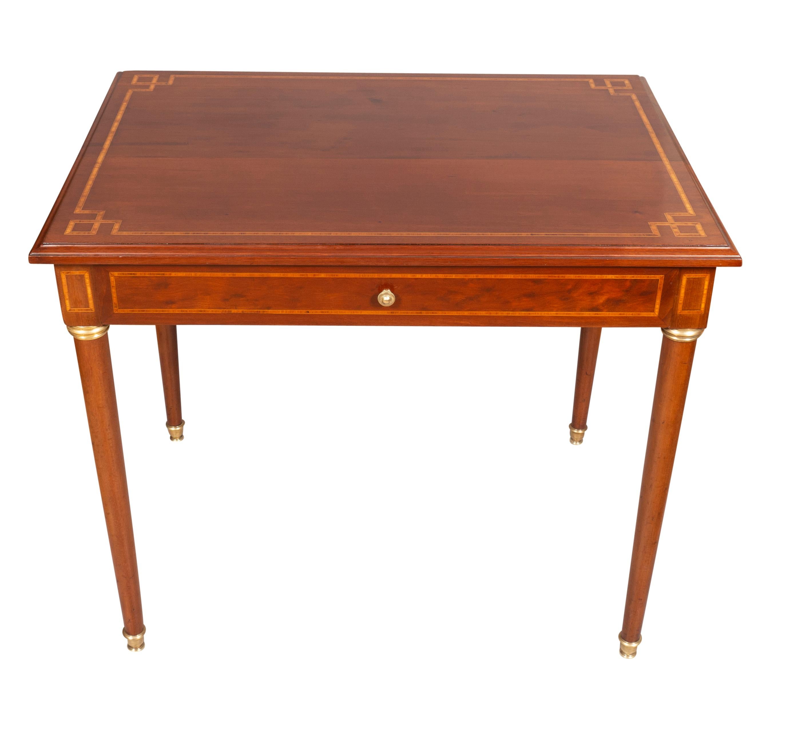 Rectangular top with inlaid border over a single long drawer and circular tapered legs headed by brass cuffs. Sabot feet.