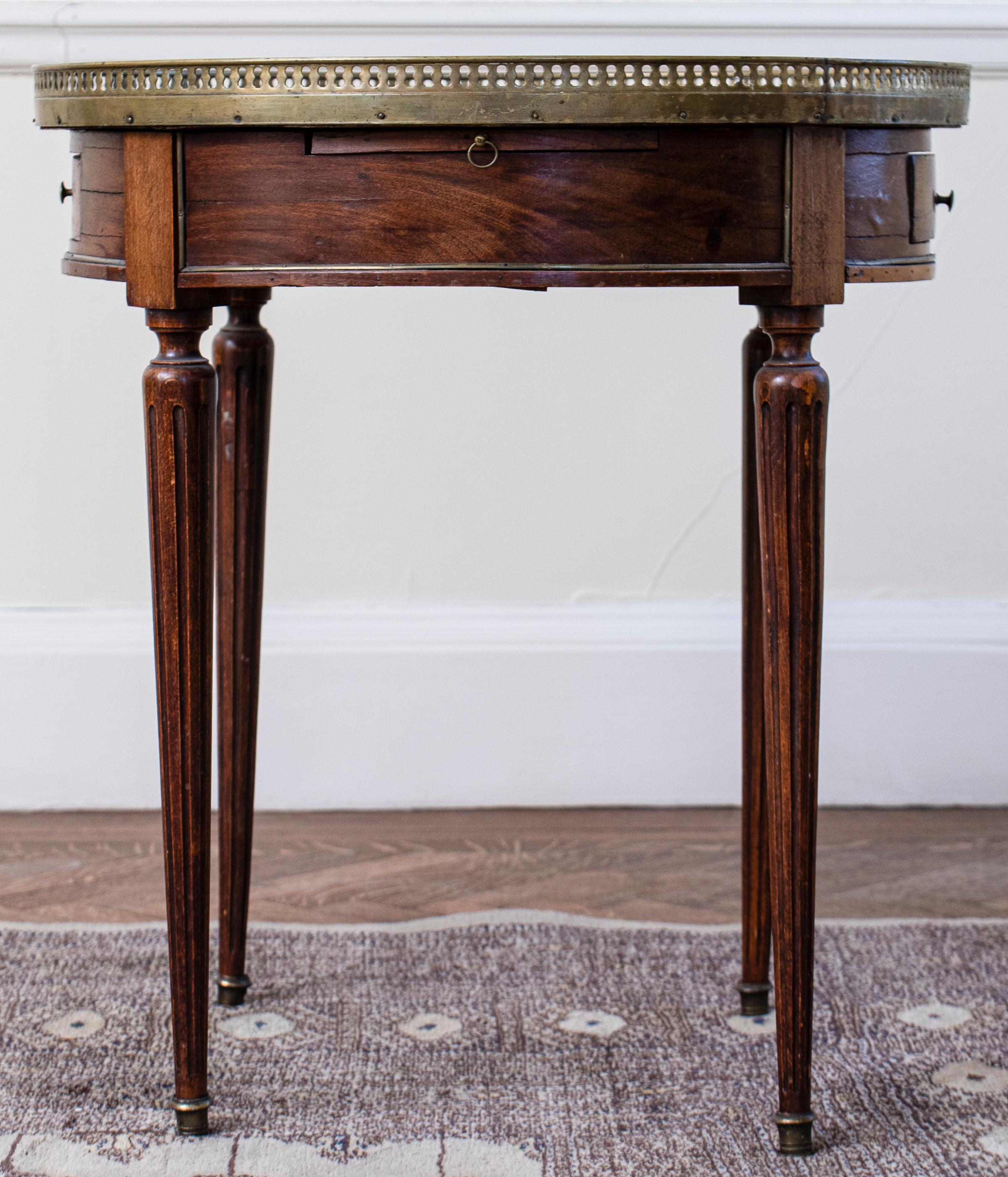 Louis XVI style gilt metal mounted gueridon, late 19th century, the white marble top within a gallery above two small drawers, raised on tapered legs on casters. 
Dimensions: 27.5