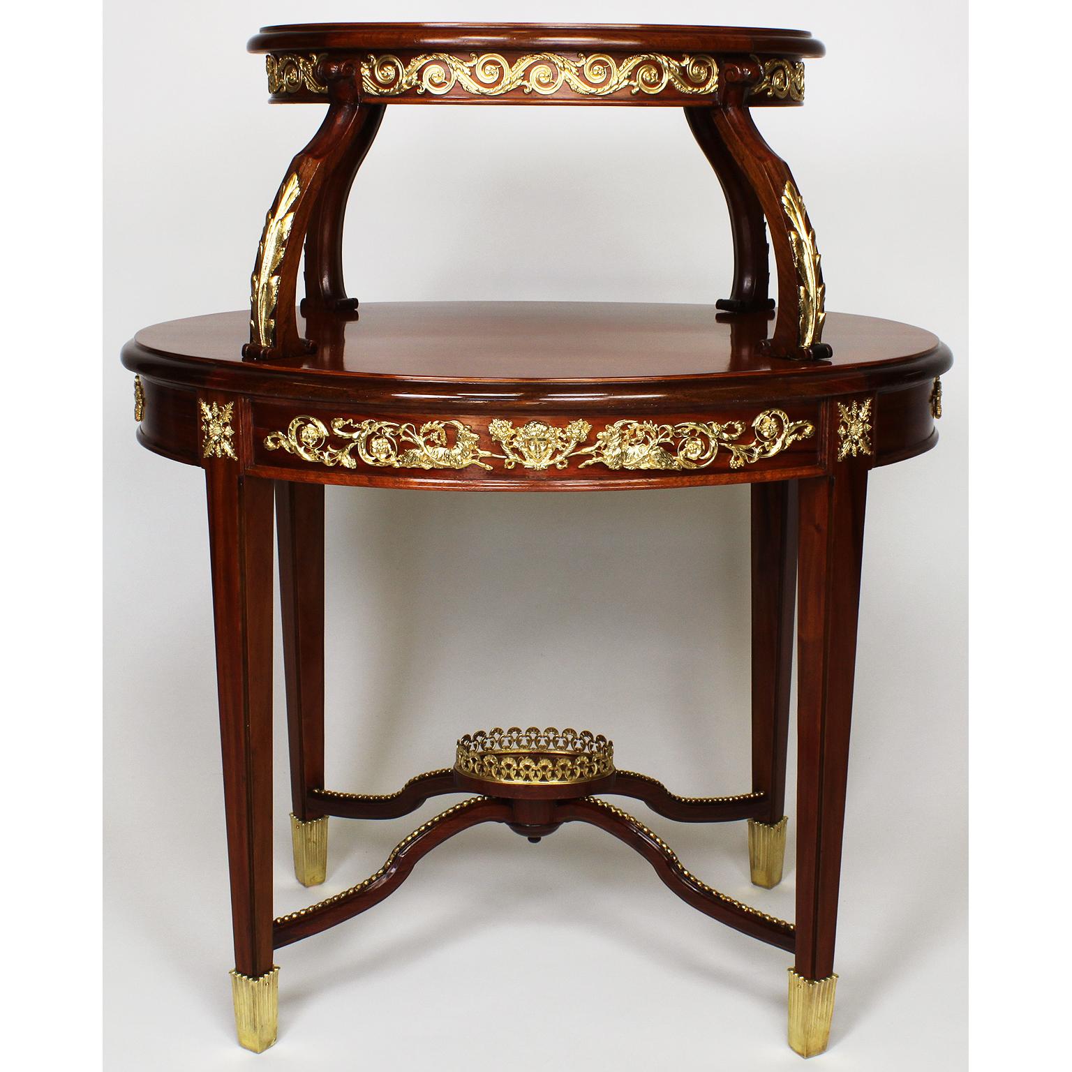 A charming early 20th century Louis XVI style mahogany, gilt bronze mounted and parcel-gilt ovoid two-tier tea or dessert table by P. E. Guerin. The twin-top dessert with quad-supports with parcel-gilt acanthus carvings, the aprons with gilt bronze