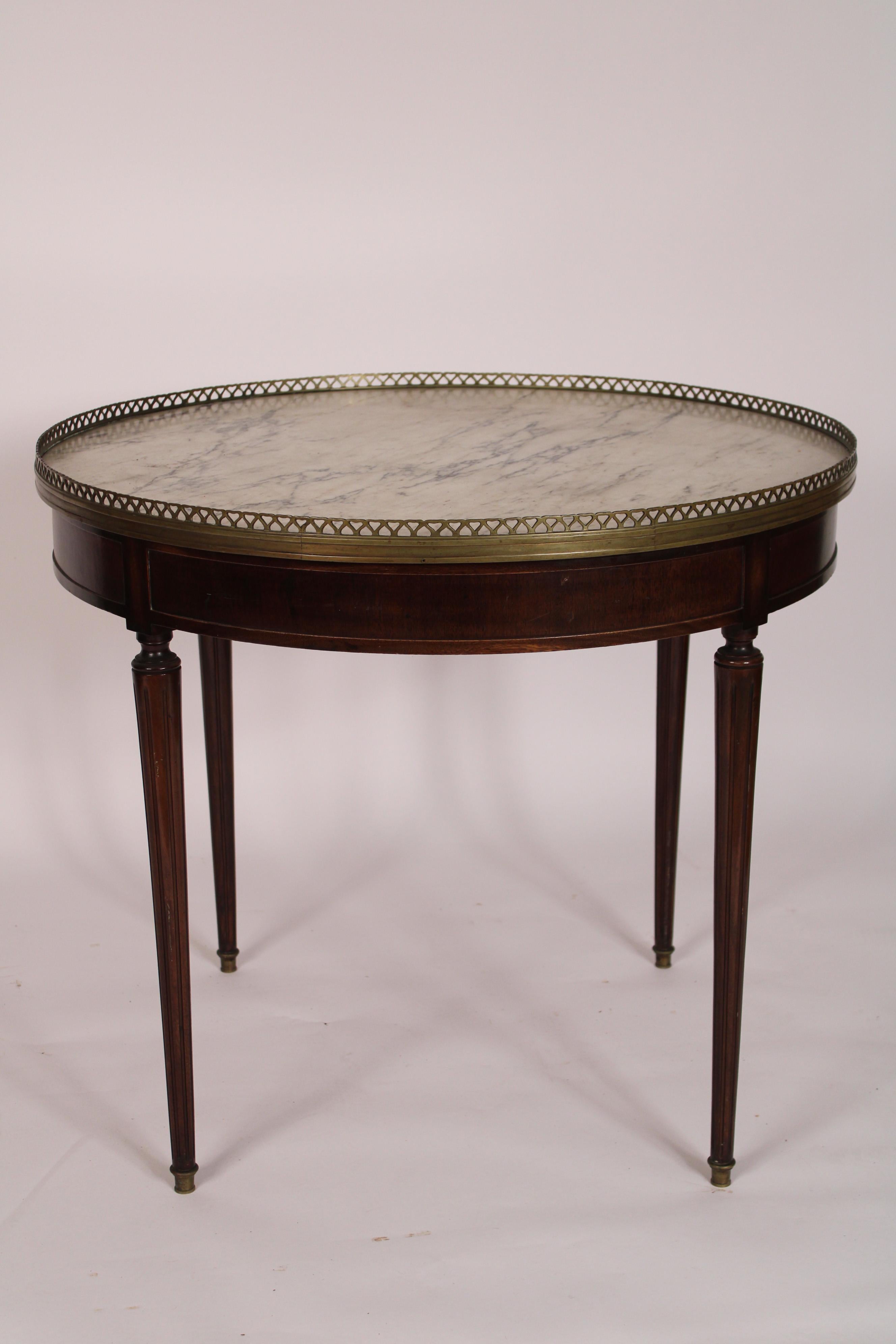 Louis XVI style bouillotte table, circa 1930-1940. With a marble top bordered by a pierced brass gallery, a frieze with two pull out candle slides, resting on turned fluted
 tapered legs ending in brass sabots. Height of gallery 28.5