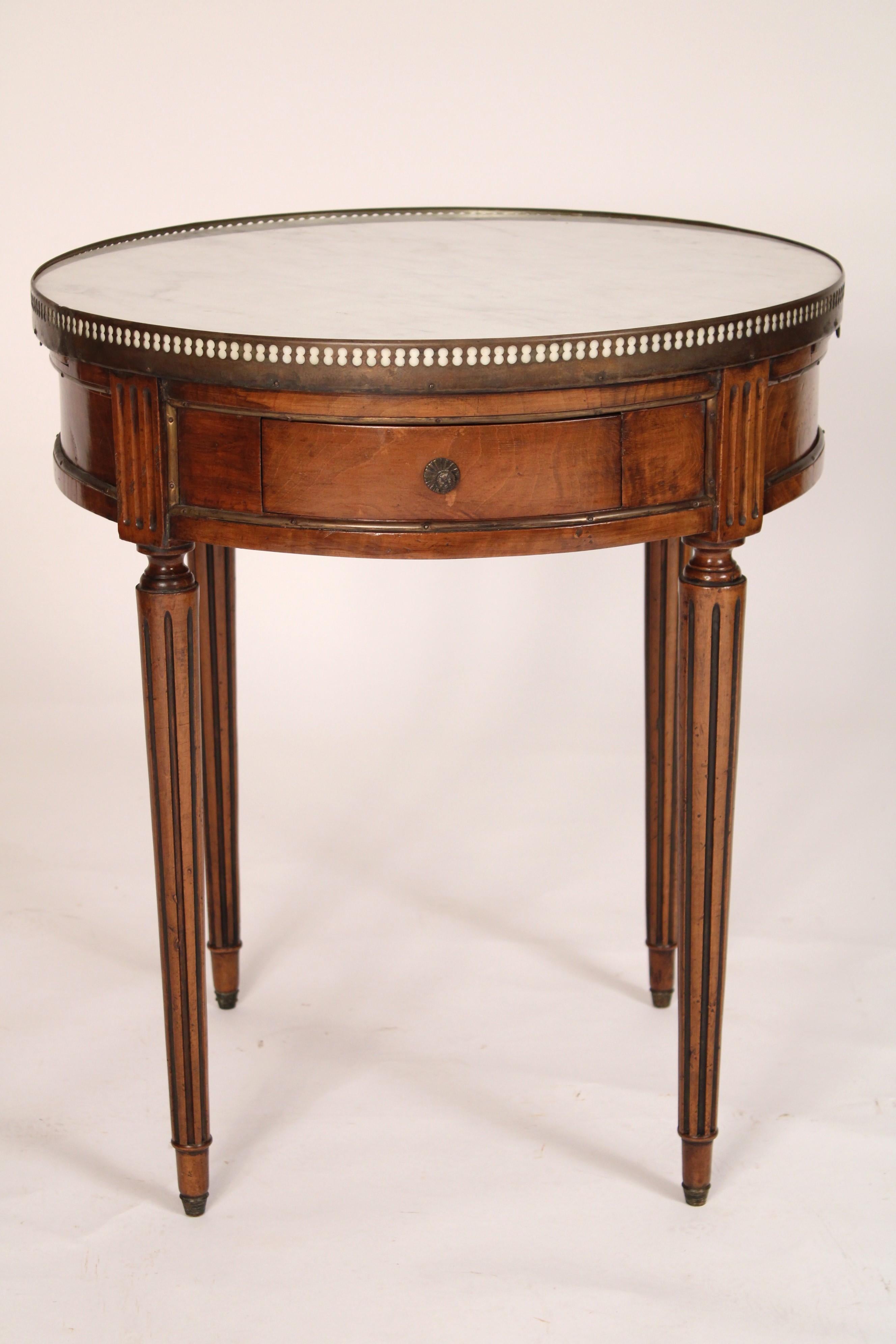 Table bouillotte en acajou de style Louis XVI, vers 1930. Le plateau à galerie réticulée en laiton et plateau de marbre de Carrare rapporté, la frise à moulures en laiton, deux tiroirs et deux écritoires reposant sur des pieds tournés et fuselés. 