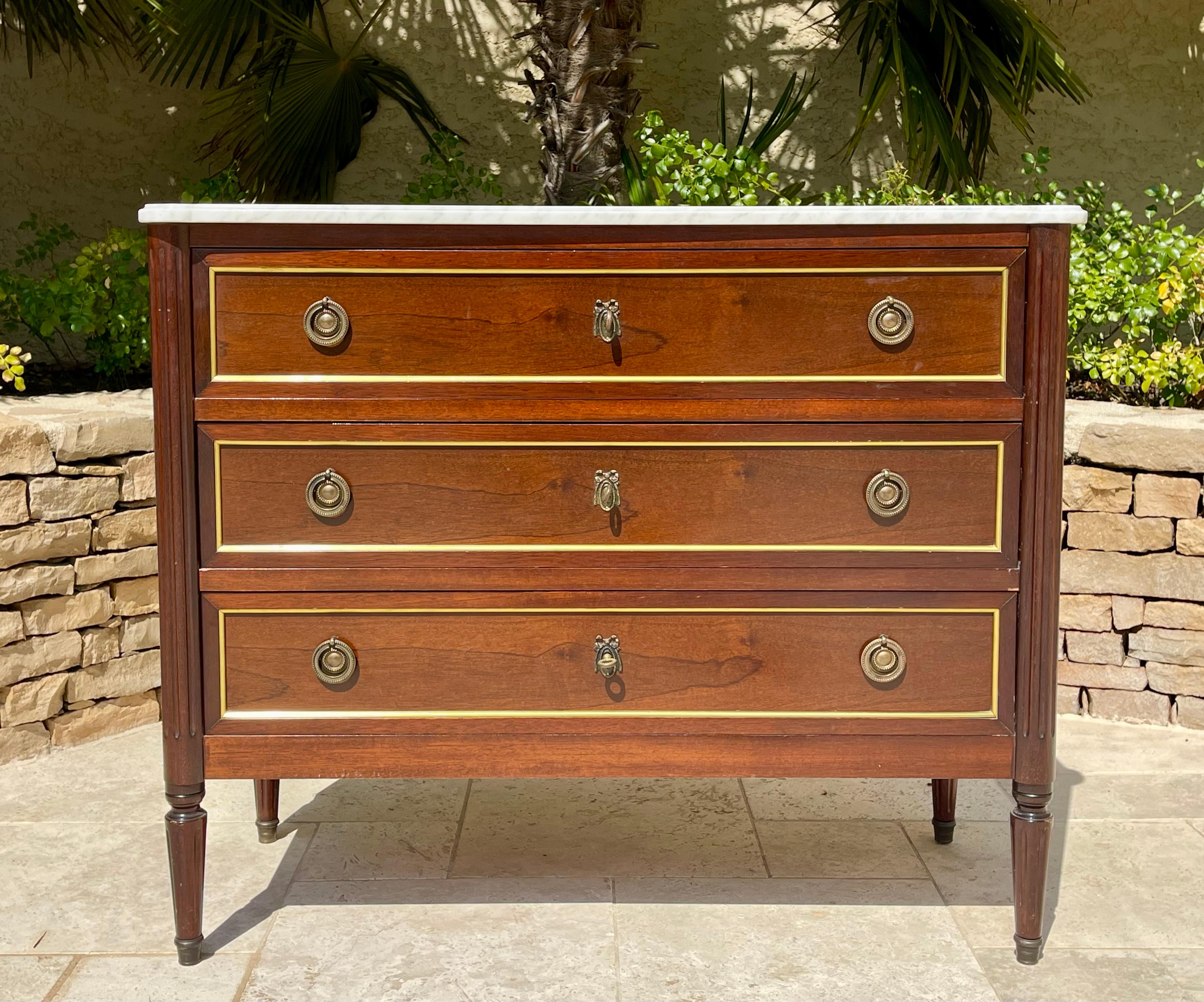 Louis XVI style mahogany and bronze chest of drawers. It has three drawers and the top is covered with original white marble in good condition. Very elegant chest of drawers in good condition. Circa 1950. 
 
 Dimensions
 Height 85cm, Width 1m02,