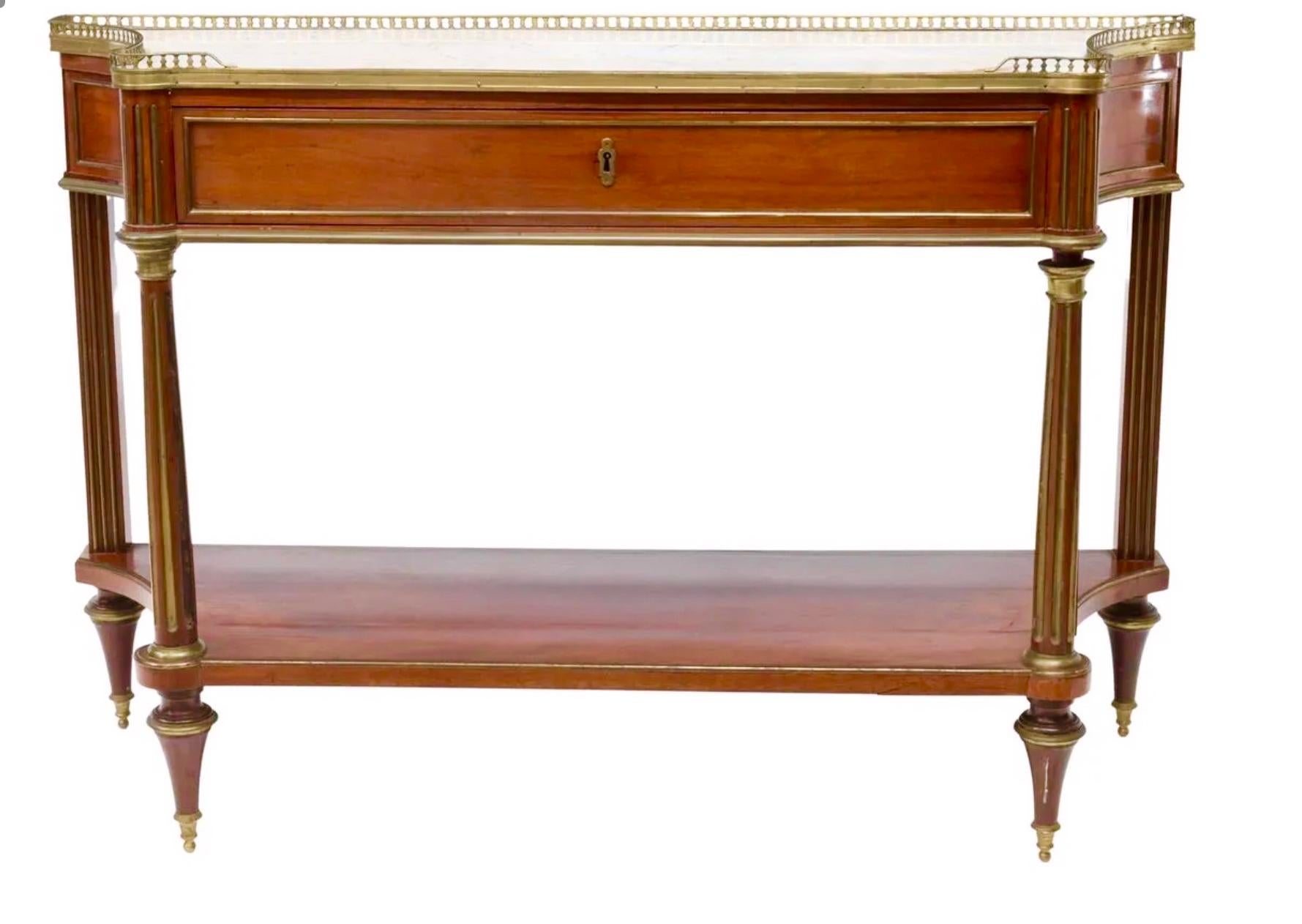 With fluted legs and brass top gallery. Good rich color and patina. Lower shelf with age crack ( stabilized ). Scalloped sides. Toupie feet and with key .

Sturdy. Tarnish to brass fittings. Separation ( crack ) to lower shelf. Dents and dings to