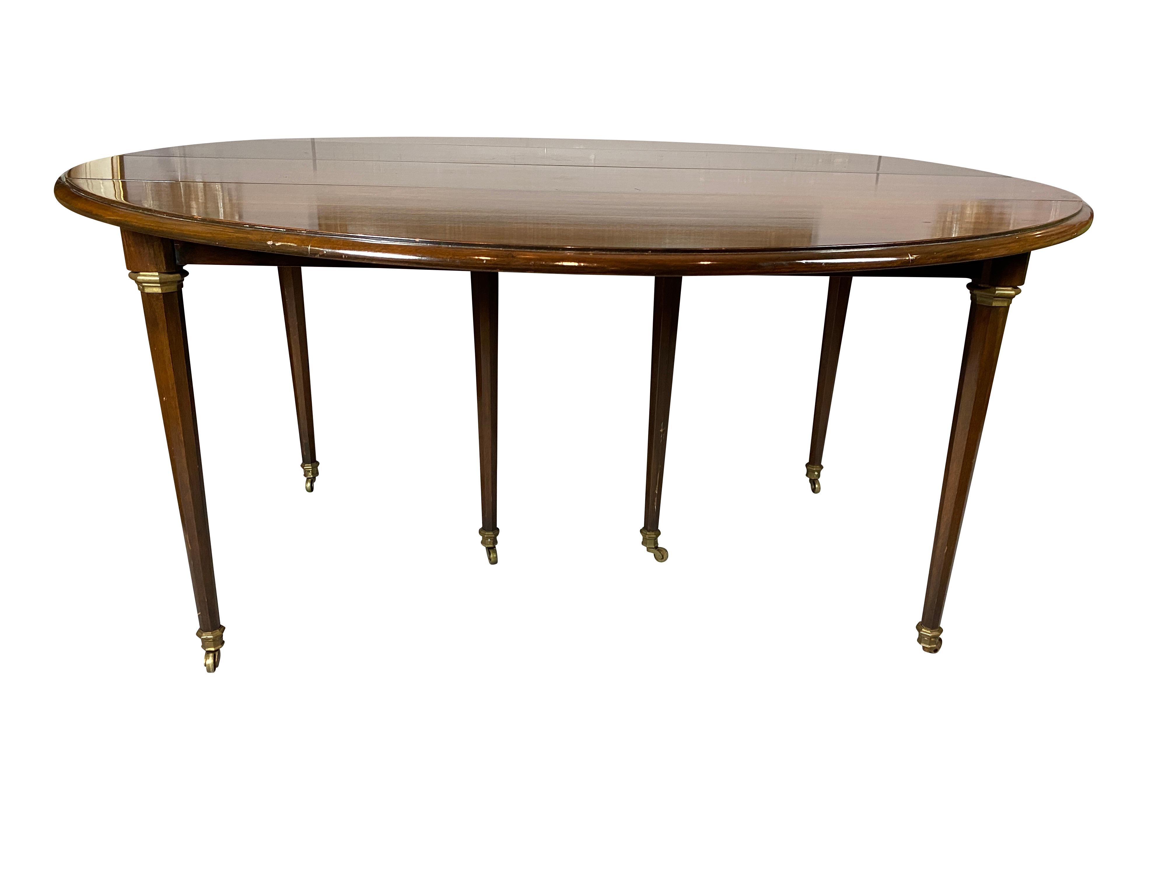 Probably by Jansen. With drop leaf ends , circular when closed with three leaves , brass cuffs on tops of legs. Leaves supported by telescoping mechanism circular tapered shaped legs ending on casters.