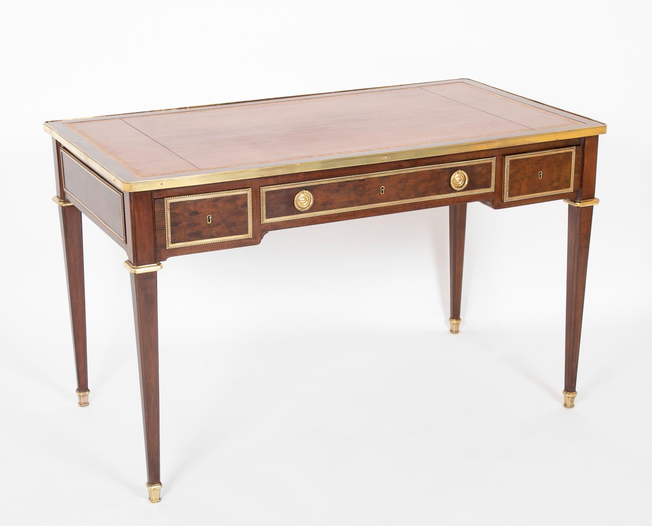 Mahogany and mahogany veneer rectangular flat desk opening to three drawers in front. Tapered legs chamfered on the corners. Finely chased and gilded bronze ornaments with rows of pearls underlining the mahogany panels, leather covered top, and