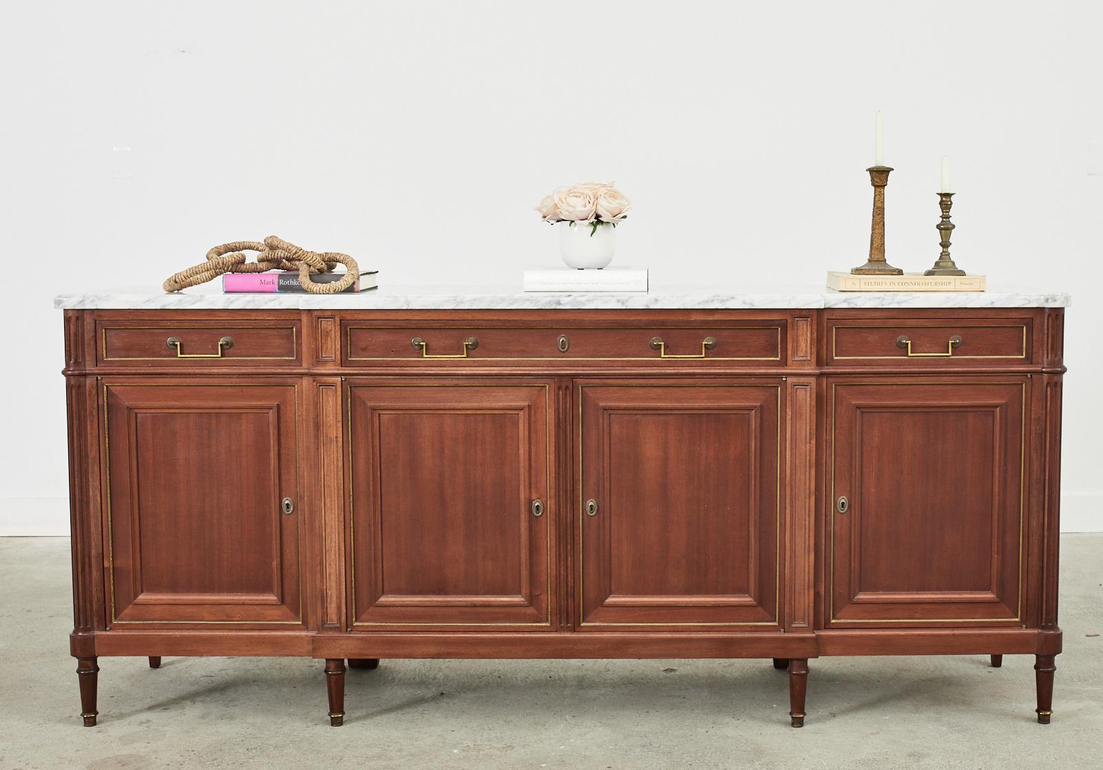 Distinctive French mahogany enfilade sideboard server or buffet featuring a thick Italian Carrara marble top. The rectangular mahogany case is fitted with four storage doors in an enfilade style. The doors and drawers are fitted with bronze