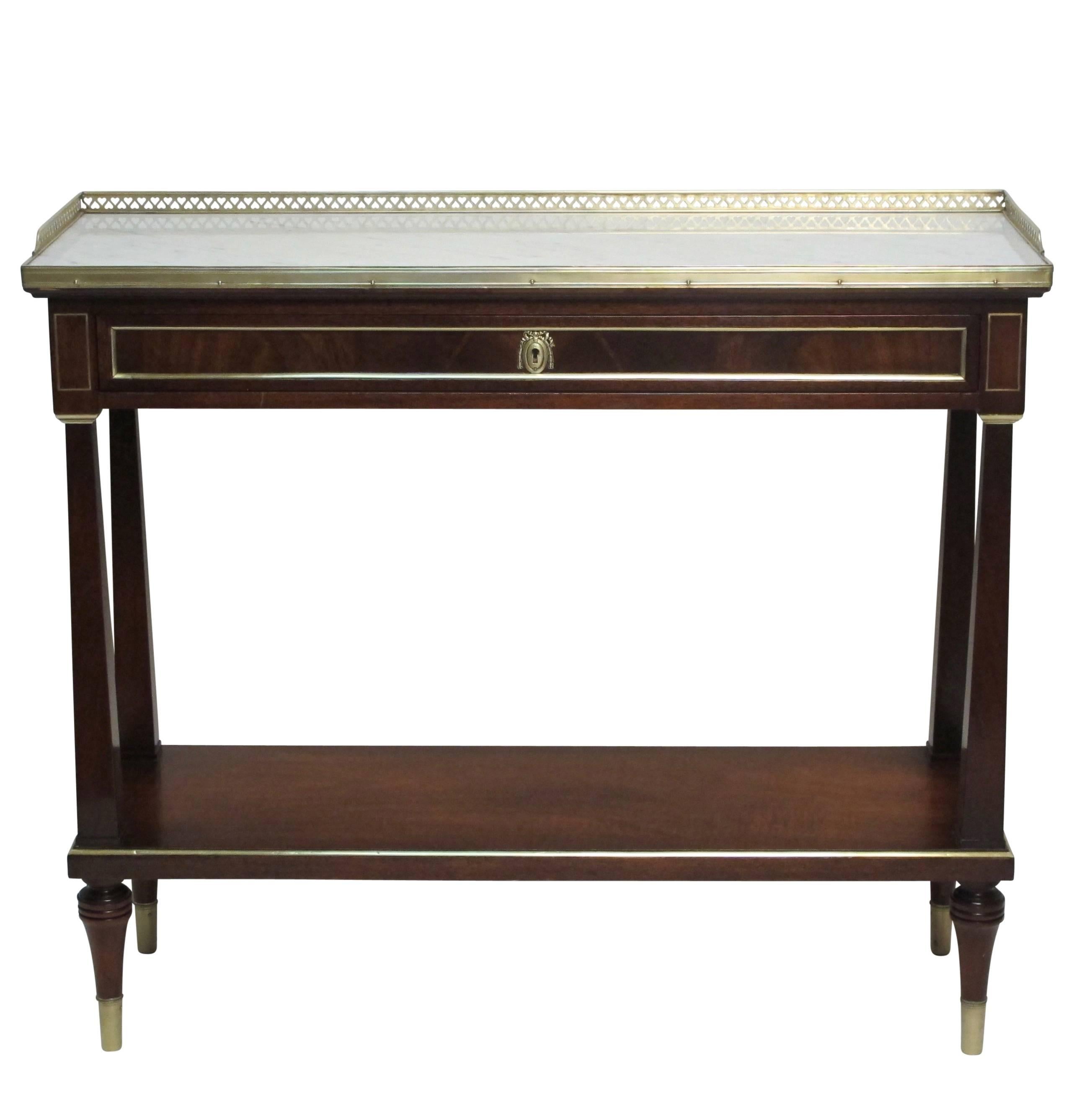 A Louis XVI style mahogany server with brass trim, moulding, gallery, and an inset marble surface. Having a single drawer and lower shelf, standing on brass capped toupee feet in the manner of Louis XVI, American, circa 1950.