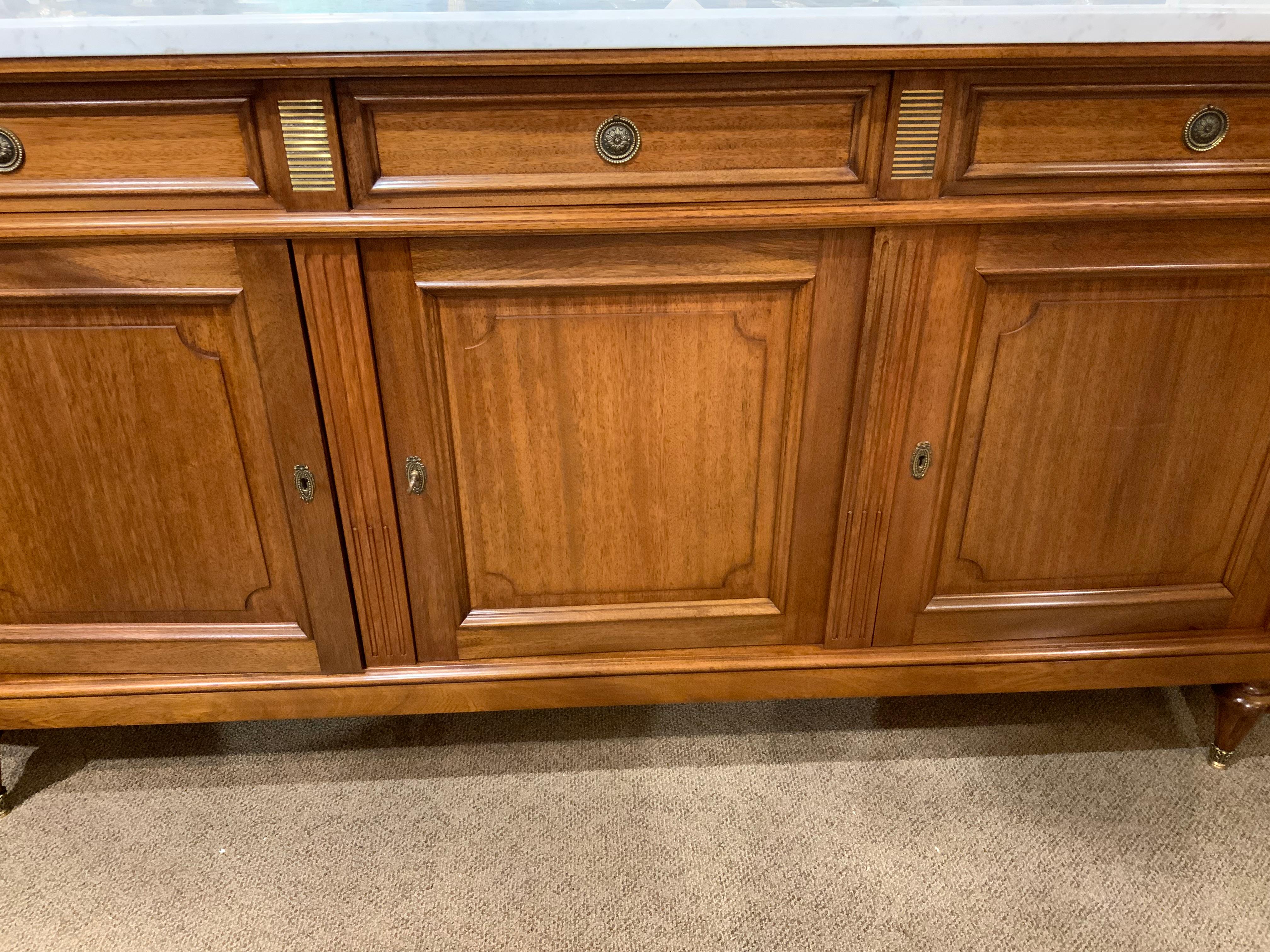Grand buffet d'excellente qualité avec de nombreux rangements.
Il s'ouvre sur cinq portes avec des étagères intérieures. Il repose sur 
Pieds cannelés de style Louis XVI. Le plateau en marbre blanc est sans 
Éclats, cassures ou réparations. Les