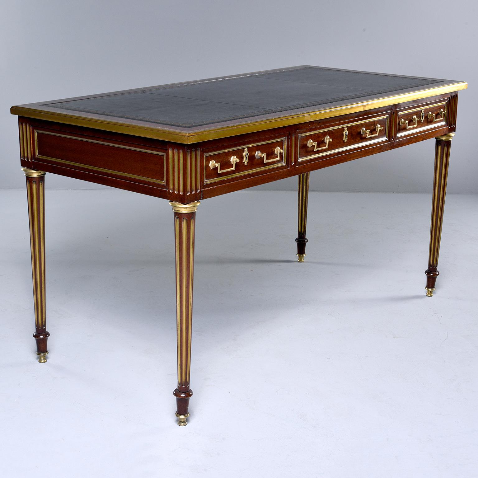 Louis XVI style mahogany desk has a new black leather top, brass trim and hardware, three functional drawers with dovetail construction, tapered, reeded and gilded legs and brass foot caps, circa 1850s. Knee height is 24.25”.