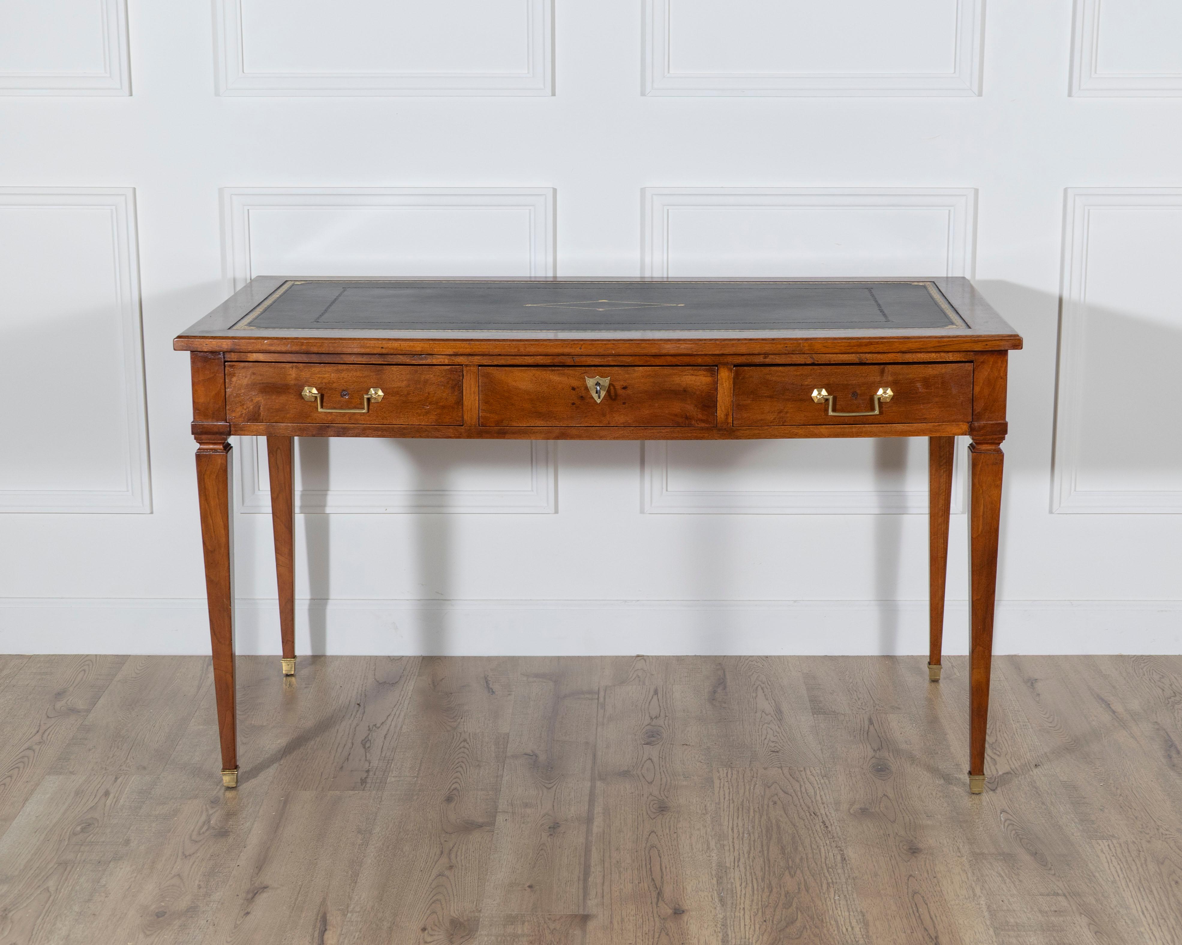 An elegant Louis XVI–style flat writing desk crafted in waxed blond mahogany, combining refined symmetry with timeless neoclassical design. The desk opens along the belt with three drawers — the central drawer fitted with a working lock and key, and